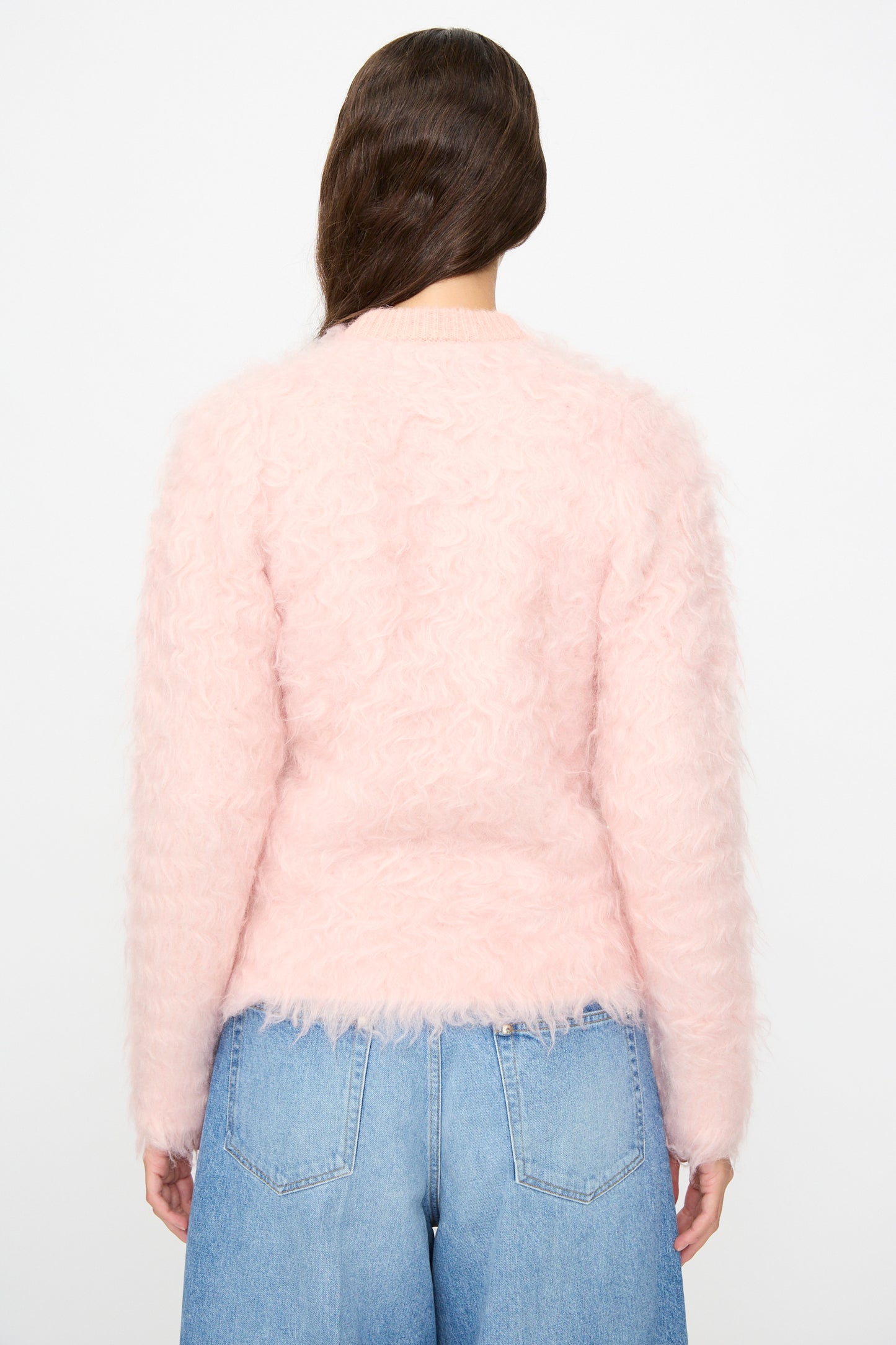 A person with long brown hair, facing away, is wearing the TOGA ARCHIVES Shaggy Knit Pullover in Pink and light blue high-waisted jeans.