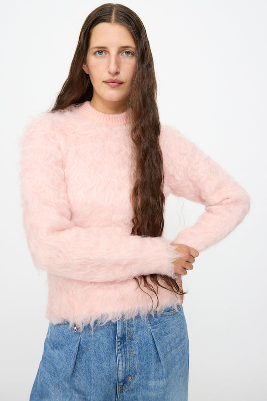 A person with long brown hair is wearing the TOGA ARCHIVES Shaggy Knit Pullover in Pink styled in a relaxed fit, paired with blue jeans and standing against a plain white background.