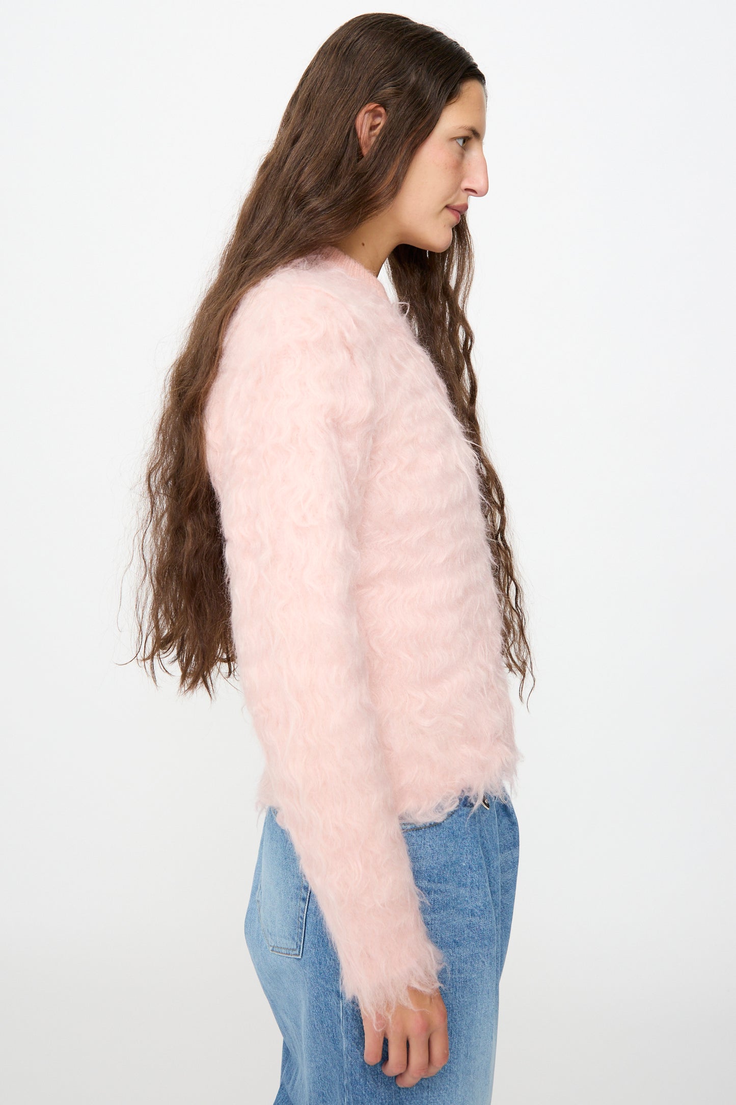 A person with long brown hair is shown in profile against a plain white background, wearing blue jeans and the TOGA ARCHIVES Shaggy Knit Pullover in Pink.