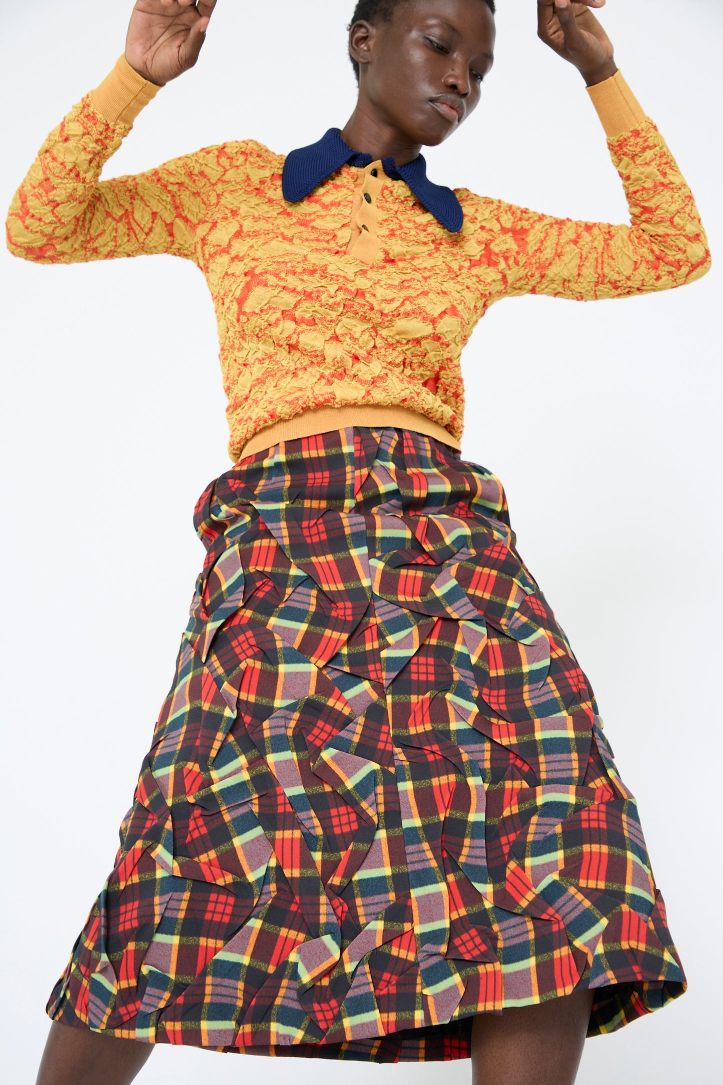 A person wearing a textured, long-sleeve yellow top with a blue collar with TOGA ARCHIVES' Twill Plaid Skirt in red. 