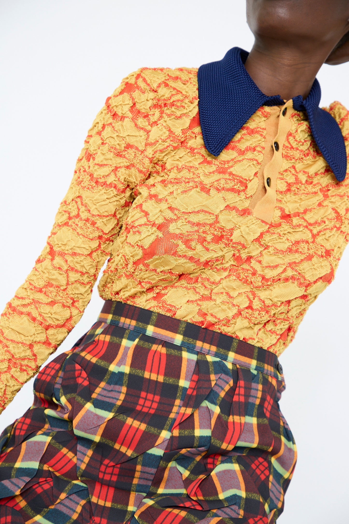 A person wearing a yellow lace top with a blue collar and a high-waist red plaid midi skirt from the TOGA ARCHIVES collection.