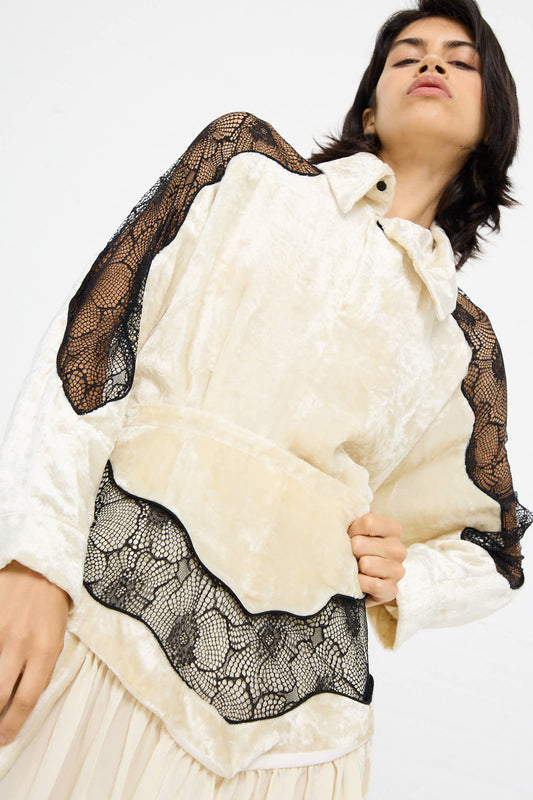 A person wearing the Velvet Lace Shirt in Off White by TOGA ARCHIVES, featuring intricate black lace detailing, stands against a plain background.