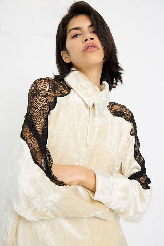 Woman in a Velvet Lace Shirt by TOGA ARCHIVES, in off white with black lace shoulder details, poses with arms crossed and a slightly tilted head.