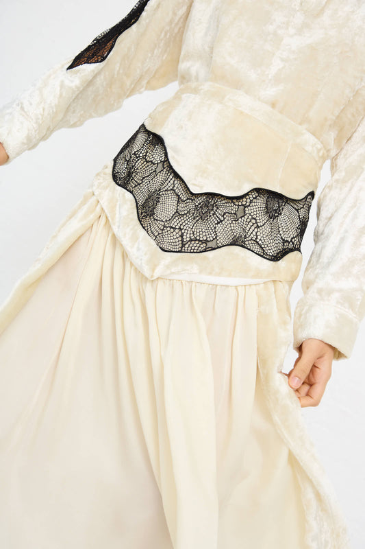 Person wearing the Velvet Lace Skirt in Off White by TOGA ARCHIVES. The skirt showcases black lace detailing and is paired with a dress featuring a fitted bodice adorned with Western motif embroidery and a flowing skirt.