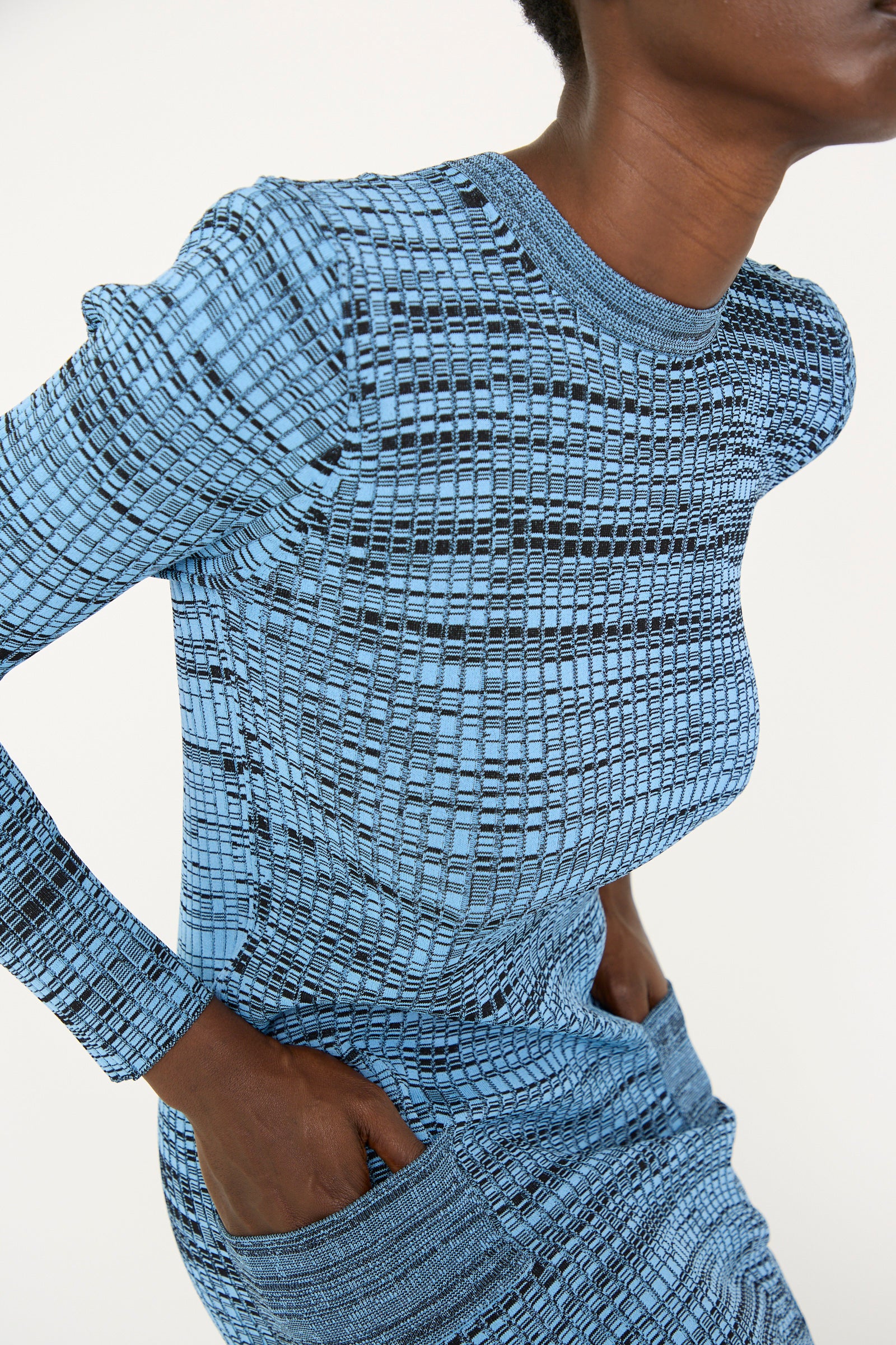 An person in a Wide Rib Knit Dress in Light Blue by TOGA ARCHIVES, with hands in pockets, posing against a plain background.