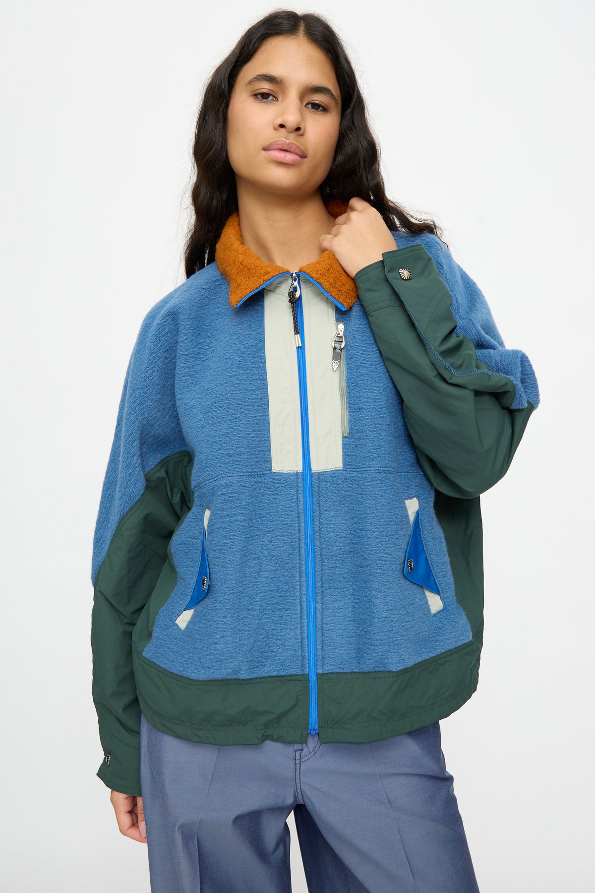 A person wearing the TOGA ARCHIVES Wool Jersey Blouson in Light Blue, a relaxed-fit zip-up jacket with tan and blue accents, made in Japan, stands against a plain white background.