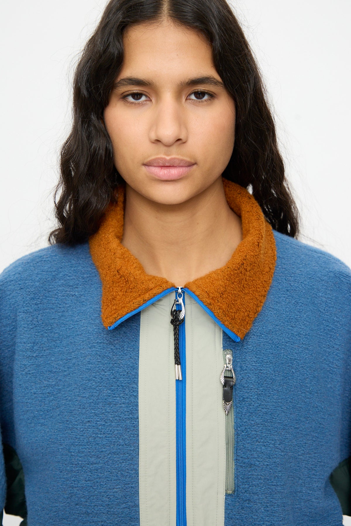 A person with long, wavy dark hair wears the TOGA ARCHIVES Wool Jersey Blouson in Light Blue—featuring a relaxed fit, brown collar, and light gray vertical stripe—made in Japan, facing forward against a plain background.