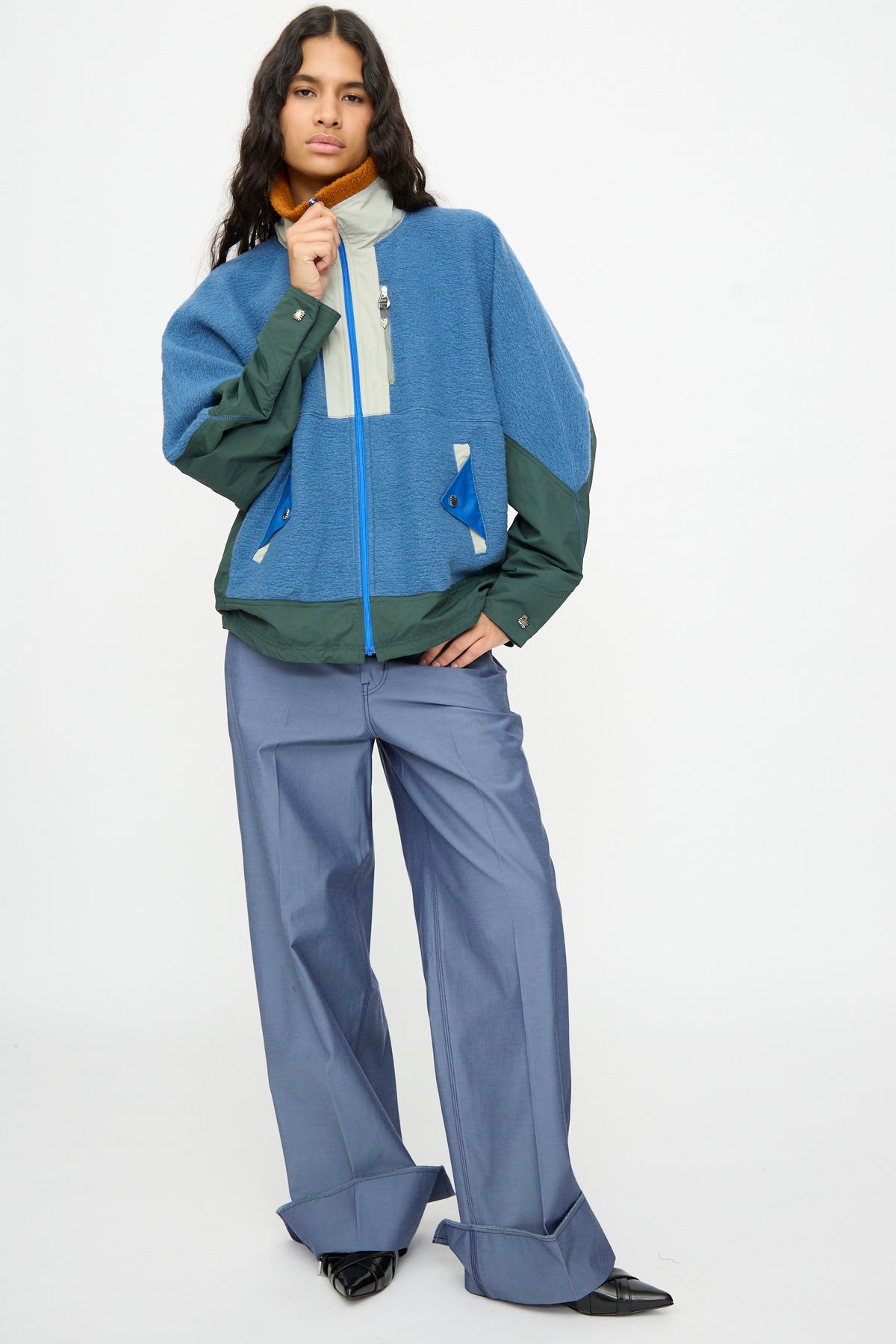 A person stands in the Wool Jersey Blouson in Light Blue by TOGA ARCHIVES, paired with blue wide-leg pants and black pointed shoes against a plain white background. This stylish ensemble is expertly crafted in Japan.