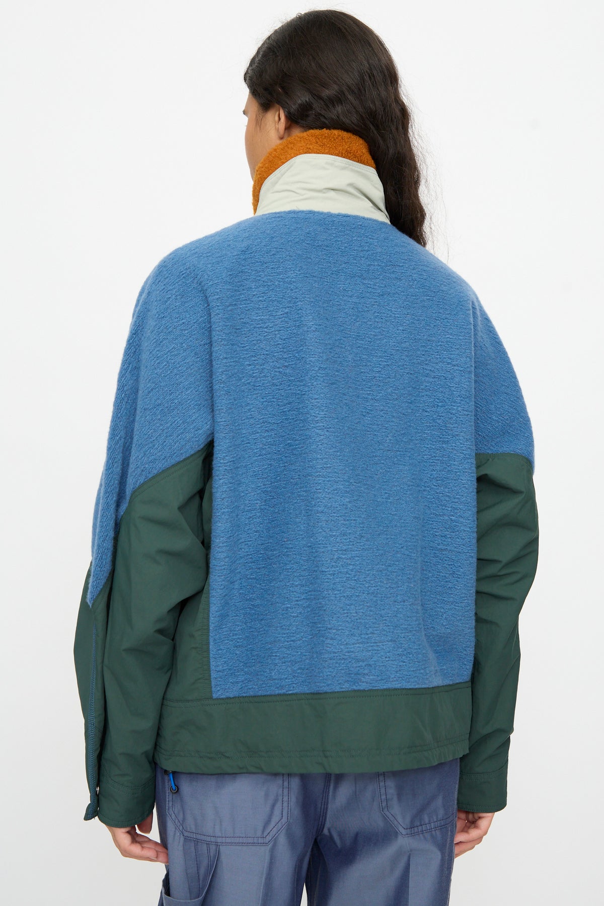 A person with long dark hair, facing away from the camera against a plain background, wears the TOGA ARCHIVES Wool Jersey Blouson in Light Blue paired with light blue pants. Made in Japan, this stylish jacket brings a distinctive touch to an otherwise understated look.