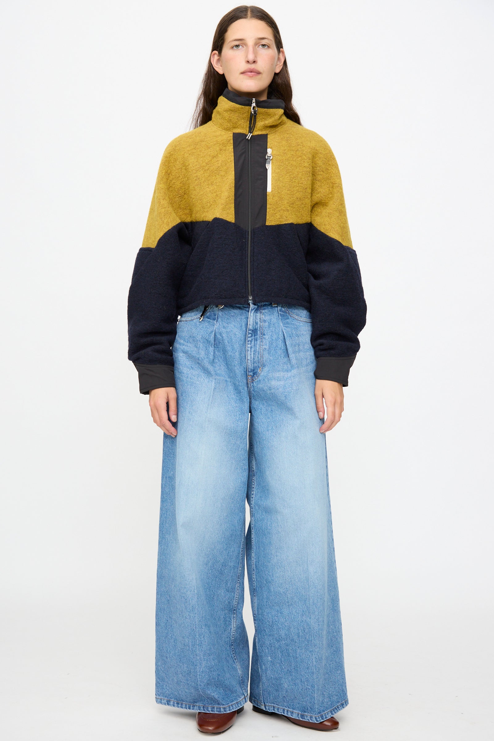 Person standing against a plain background, wearing the TOGA ARCHIVES Wool Jersey Blouson in navy, made in Japan, paired with wide-leg light blue jeans.