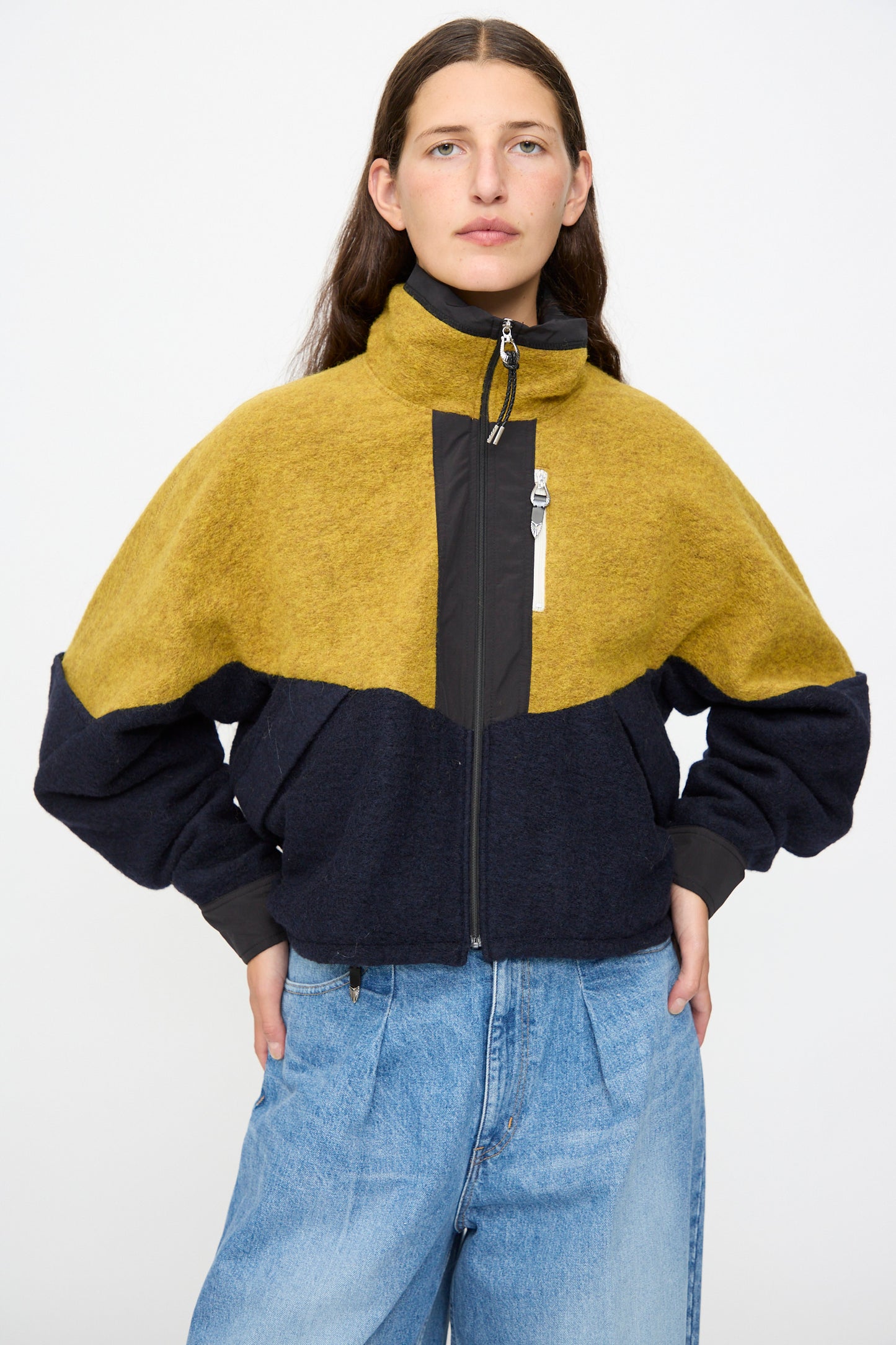 A person stands facing forward, wearing the TOGA ARCHIVES Wool Jersey Blouson in Navy—made in Japan—with light blue jeans, hands on hips, against a plain light background.