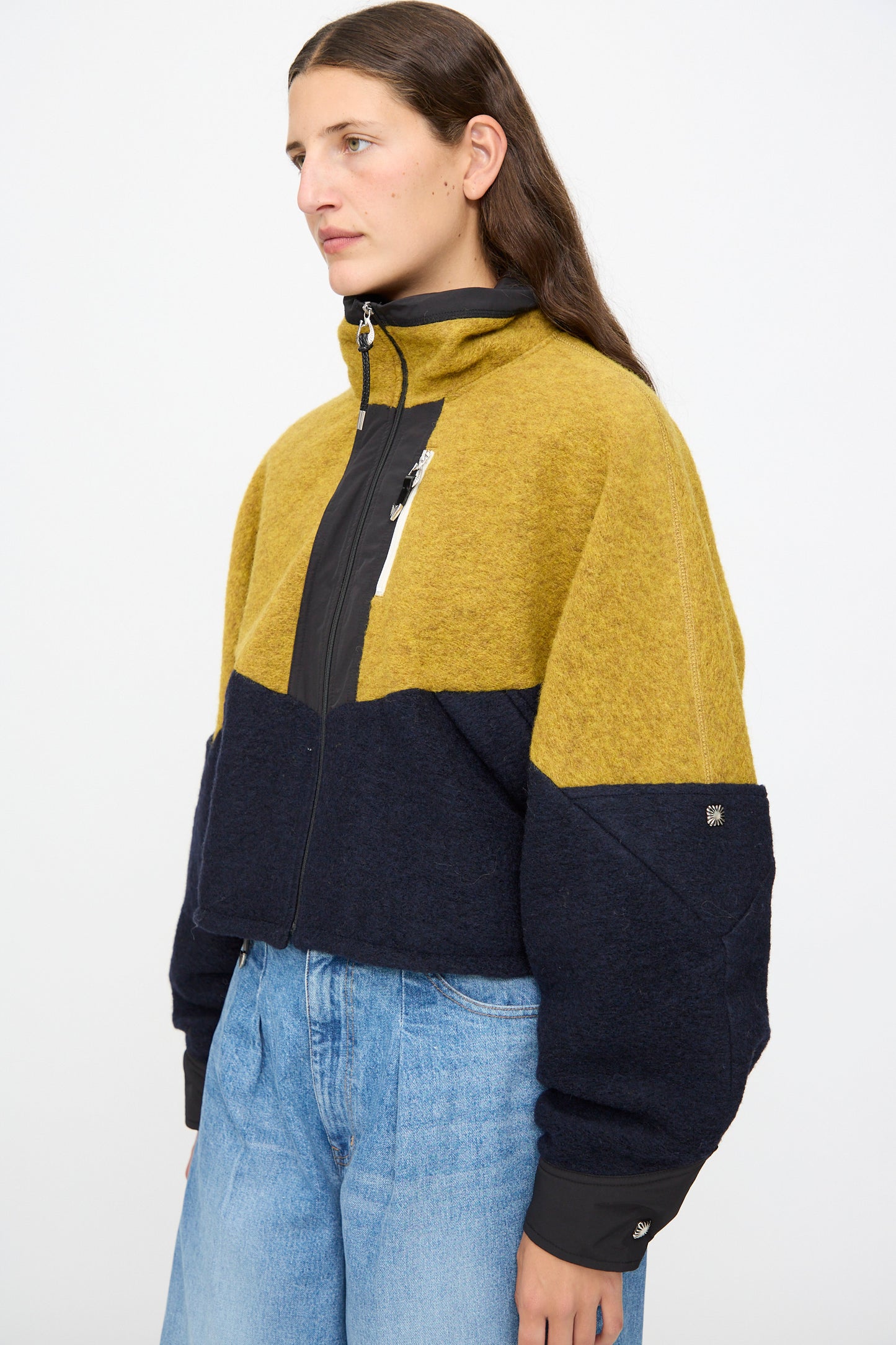 A person wears the TOGA ARCHIVES Wool Jersey Blouson in navy—a color-block cropped jacket featuring mustard yellow, black, and navy blue—paired with light blue jeans against a plain background. This stylish piece is made in Japan.