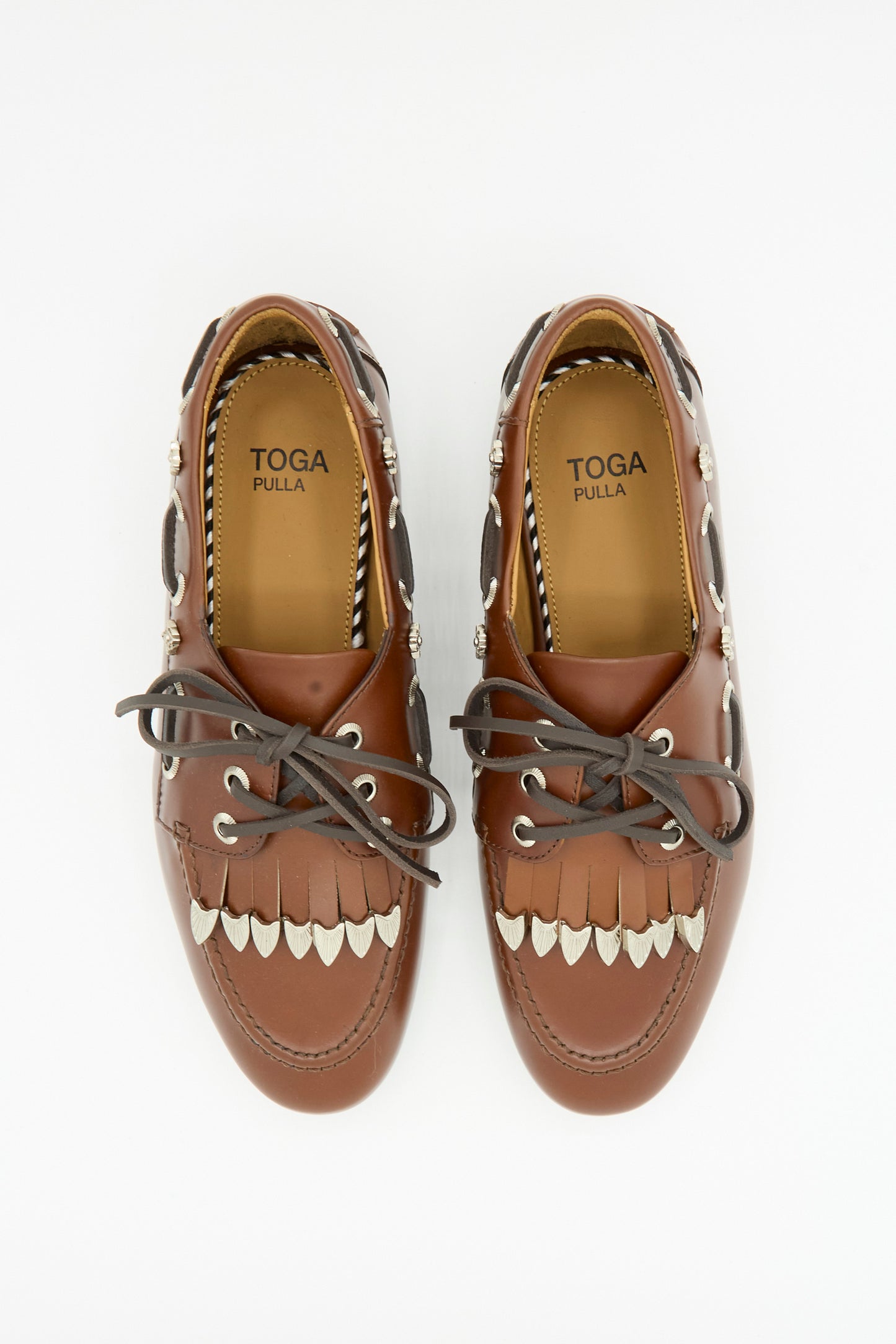 Pair of brown Leather Flat in Brown by TOGA ARCHIVES featuring decorative silver accents, fringe detail, and a classic lace-up design, photographed from above on a white background.