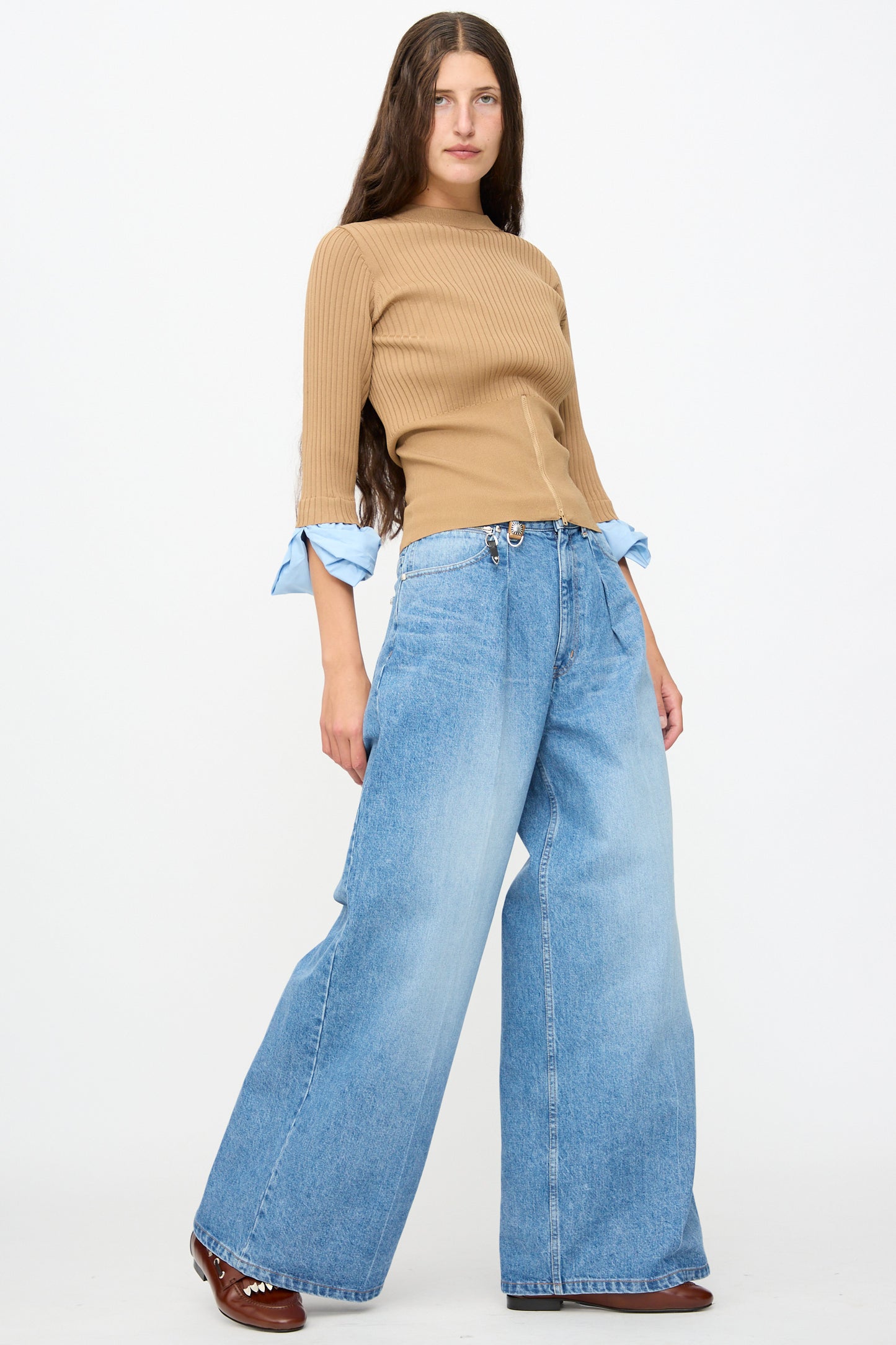 A woman wearing a tan ribbed knit top, Denim Wide Pants in Blue by TOGA ARCHIVES, and brown leather shoes.