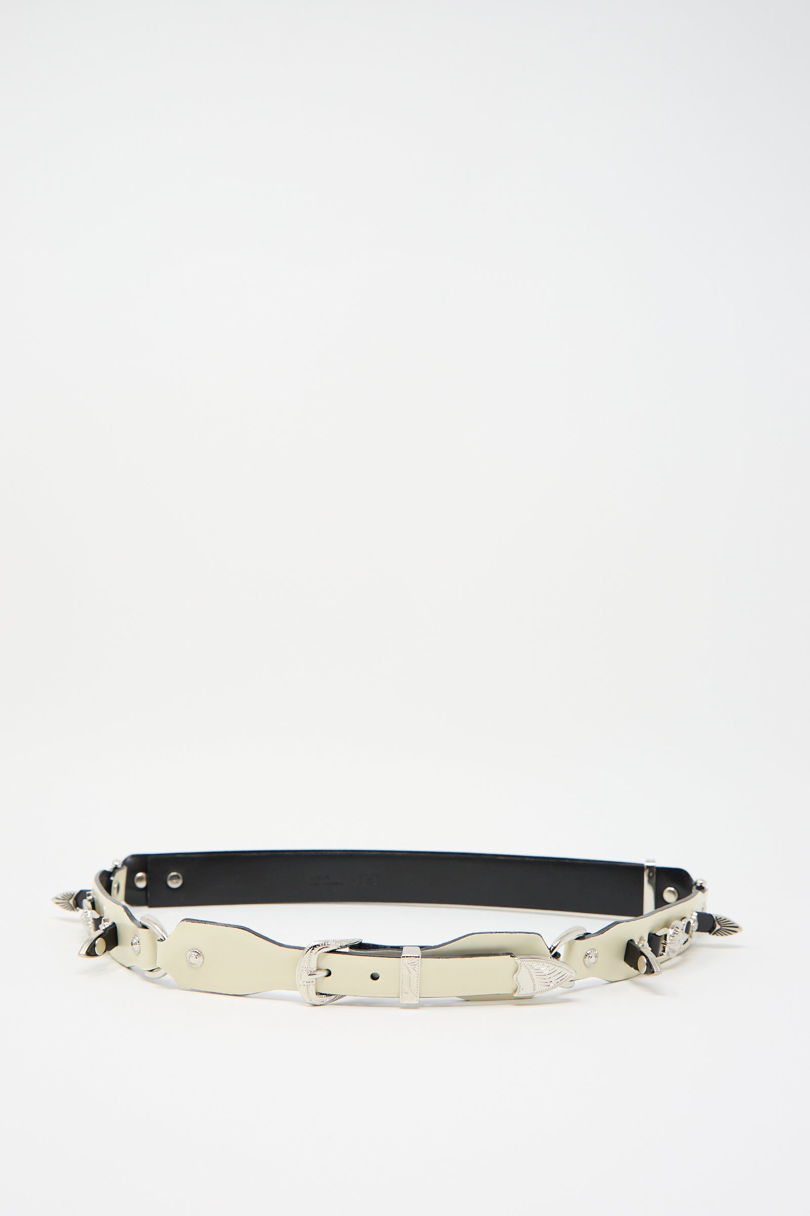 The Metal Leather Narrow Belt in Off White by TOGA ARCHIVES, featuring Western-inspired decorative elements and a metallic buckle, laid flat against a white background.