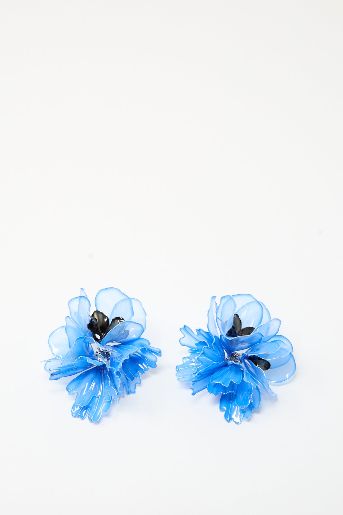 Two light blue flower earrings from TOGA ARCHIVES, crafted from translucent material with elegant black accents, are displayed on a plain white background—offering perfect inspiration for unique resin or stylish clip-on earrings.