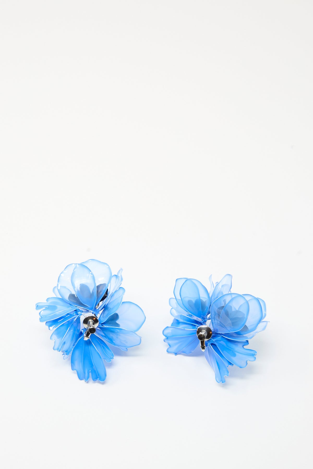 Two Flower Earrings in Light Blue from TOGA ARCHIVES, featuring silver centers and a translucent floral design, are displayed on a plain white background. These elegant resin earrings add a touch of floral charm to any outfit, and their clip-on style ensures comfortable wear for everyone.