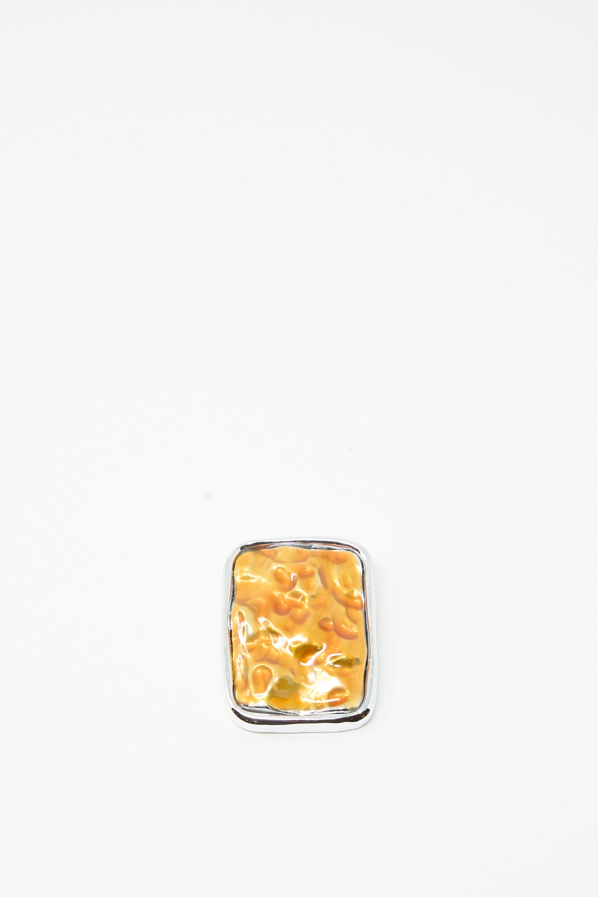 A small, rectangular brooch with an orange design from TOGA ARCHIVES, called the Square Wave Brooch, is displayed centered on a plain white background, its silver-tone brass construction giving it a quirky, baked-bean-inspired appearance; made in Japan.