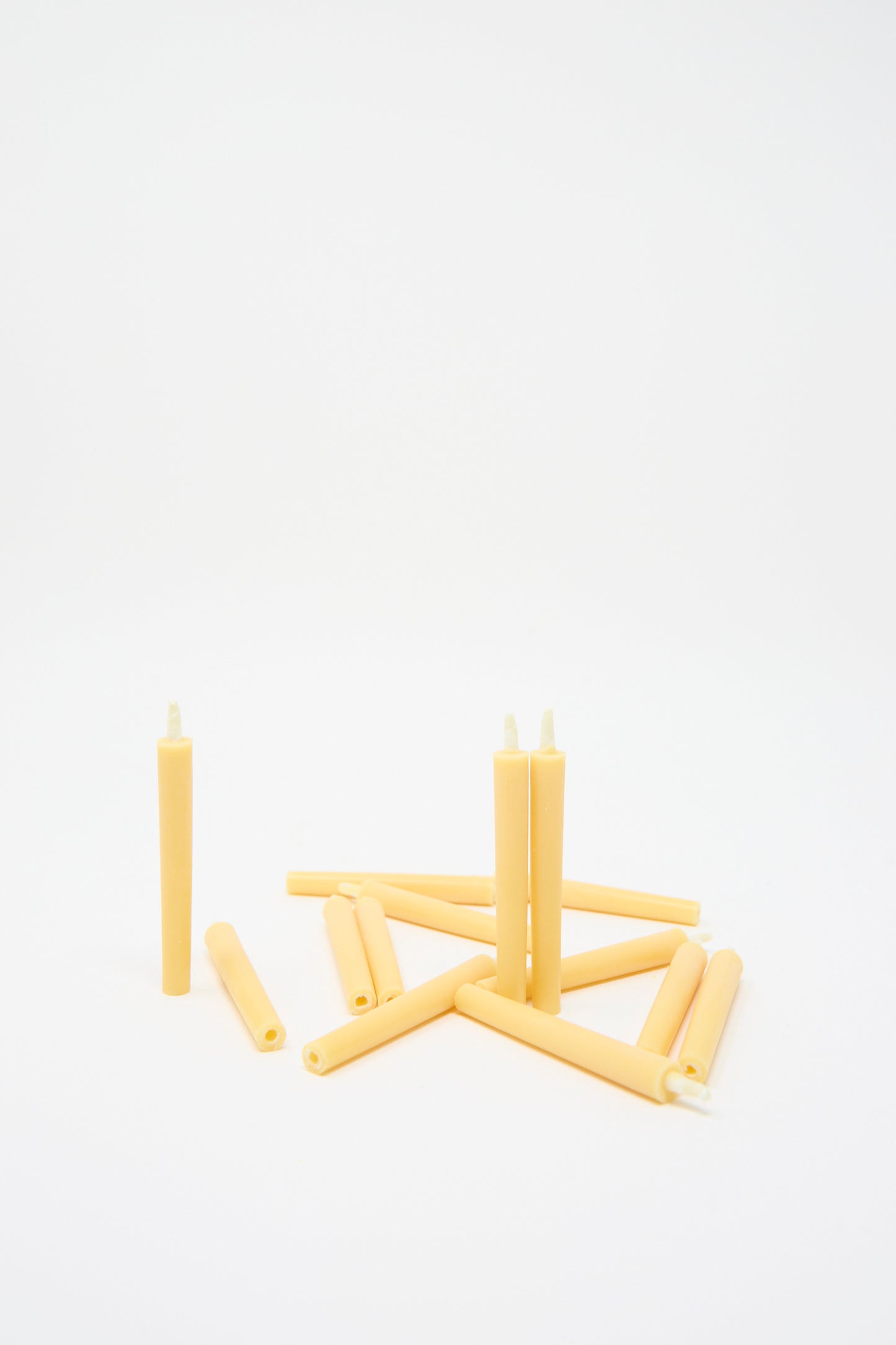 A scattered pile of Komenuka Rice Bran Candles by Saikai, inspired by 16th-century design, rests on a white background.