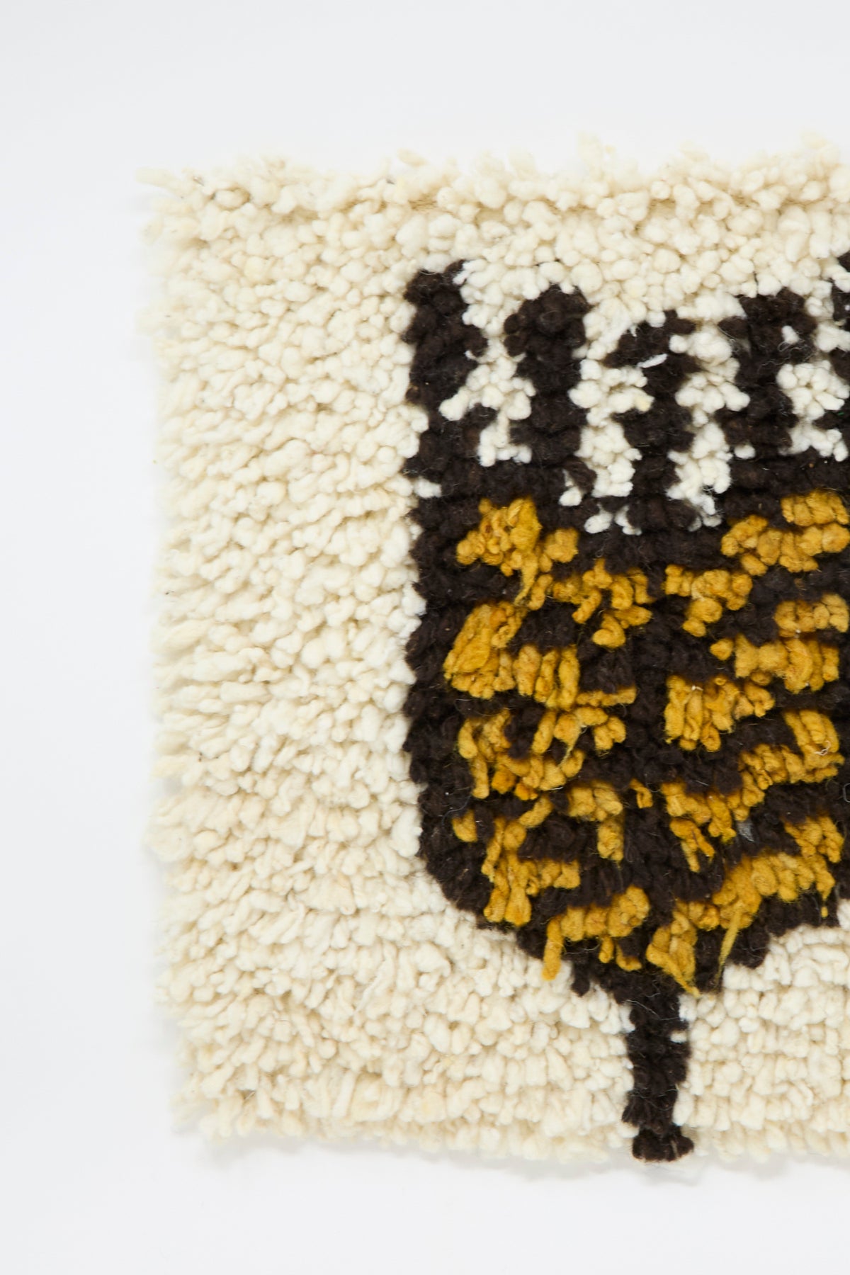 Close-up of a shaggy, off-white Tamar Mogendorff Chair Rug in Natural featuring a wheat motif in mustard yellow, brown, and white.
