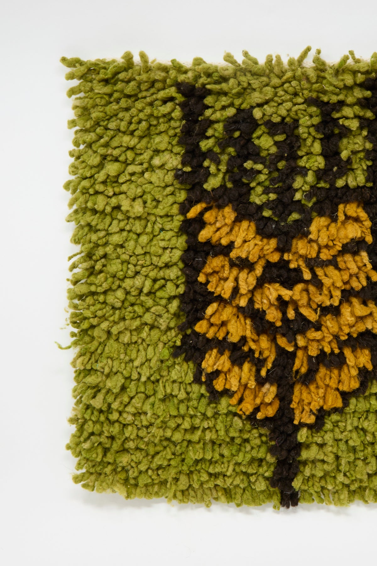 Close-up of a handwoven Chair Rug in Olive Green by Tamar Mogendorff, featuring a rectangular shag design with a green background and yellow wheat motif.