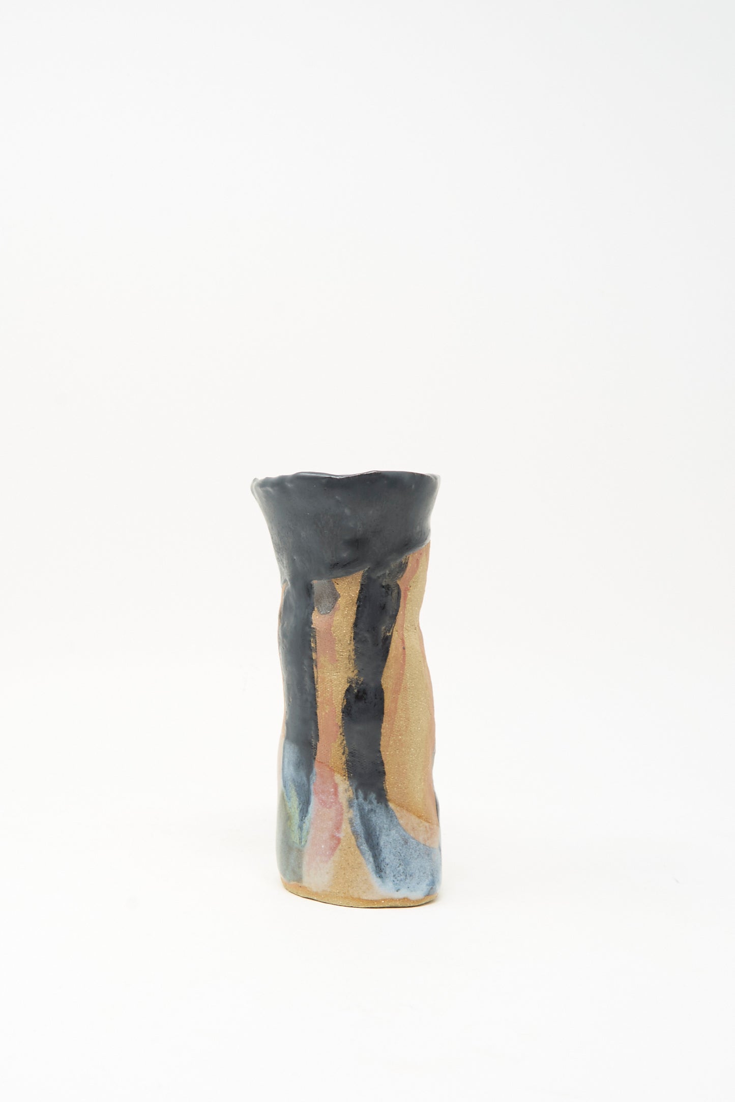 A tall, narrow ceramic candleholder with an uneven rim, featuring a tan base and abstract blue, black, and pink glaze accents on a plain white background; the "I wish I knew them Candleholder I" by Tamar Mogendorff, made in Brooklyn.