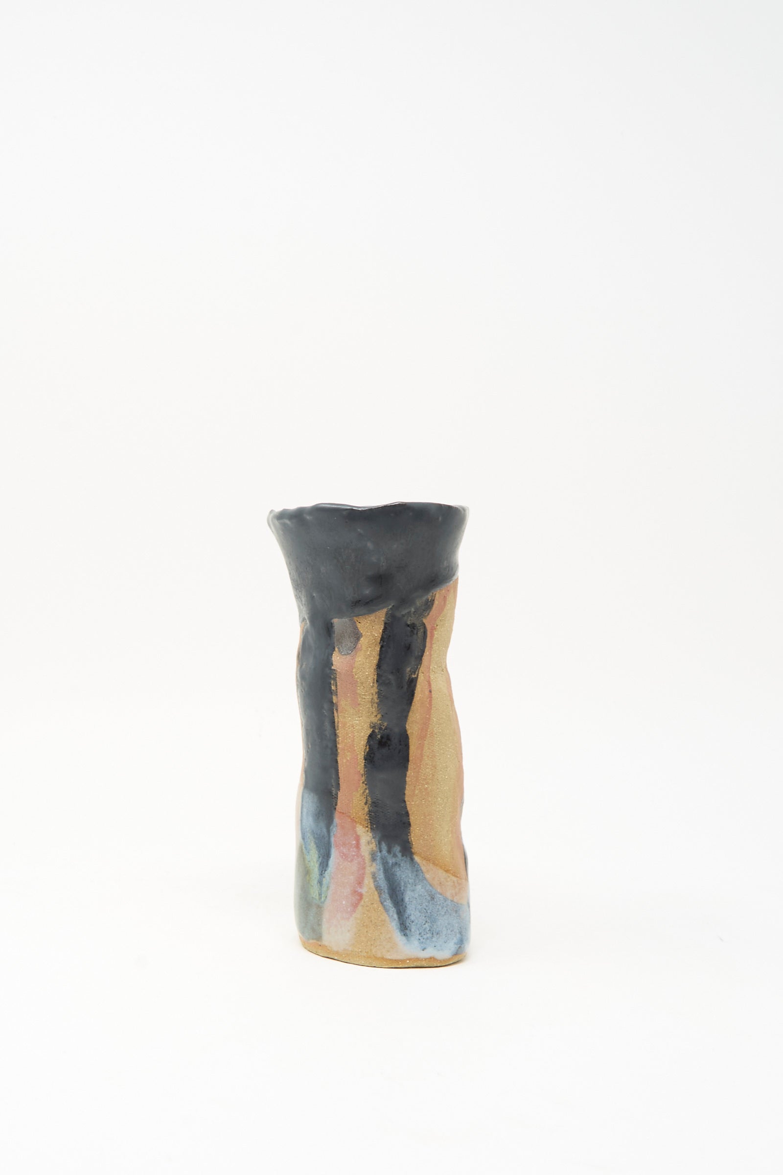 A tall, narrow ceramic candleholder with an uneven rim, featuring a tan base and abstract blue, black, and pink glaze accents on a plain white background; the "I wish I knew them Candleholder I" by Tamar Mogendorff, made in Brooklyn.