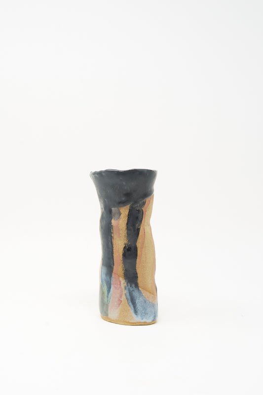 A tall, narrow ceramic candleholder with an uneven rim, featuring a tan base and abstract blue, black, and pink glaze accents on a plain white background; the "I wish I knew them Candleholder I" by Tamar Mogendorff, made in Brooklyn.
