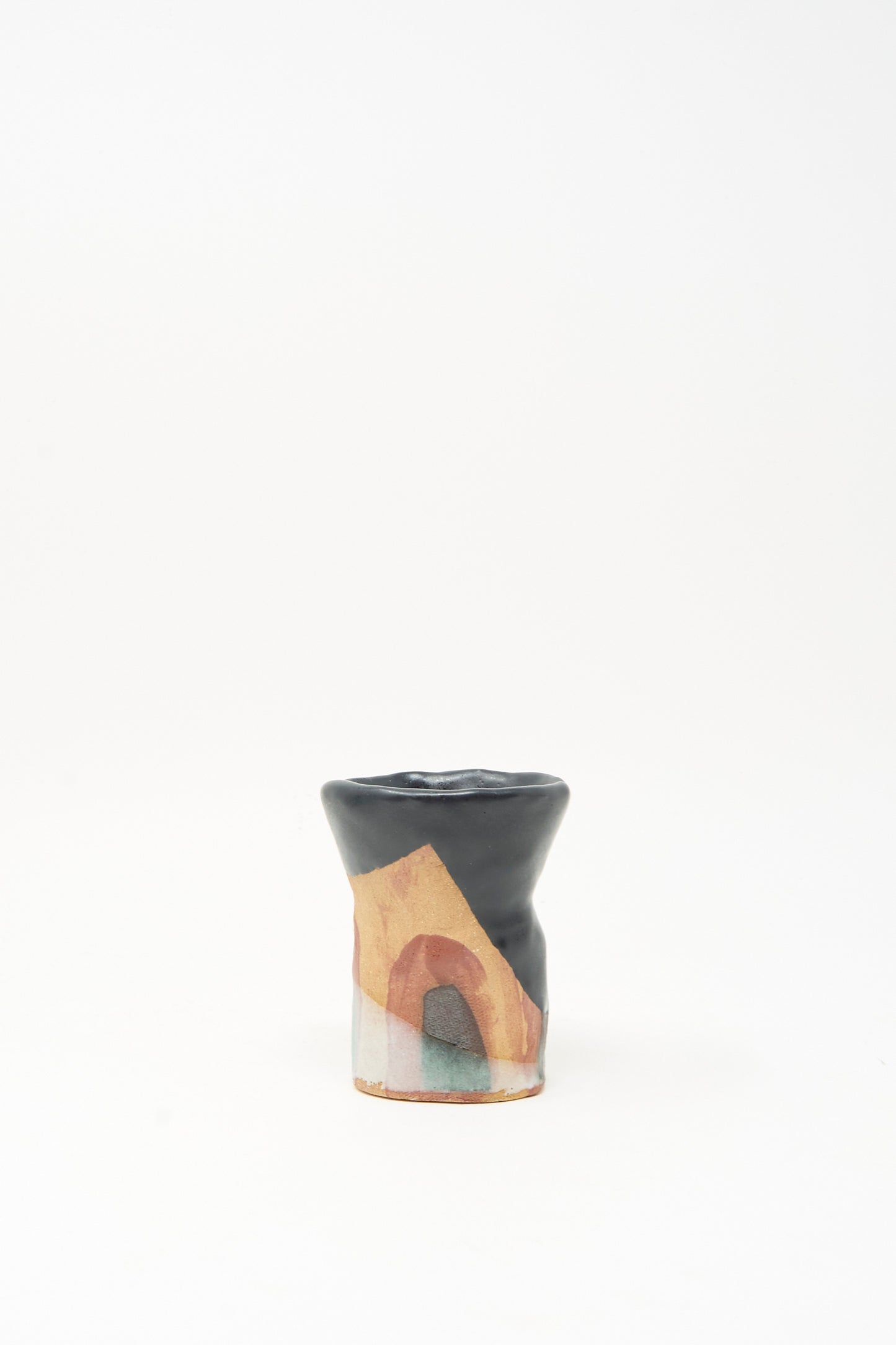 The "I wish I knew them Candleholder II" by Tamar Mogendorff is a small, uniquely shaped ceramic piece made in Brooklyn. With a black top and abstract patterns in beige, brown, and green adorning the lower half, this candleholder stands out for its artistic design. Set against a plain white background, it embodies the creative spirit characteristic of Tamar Mogendorff’s work.