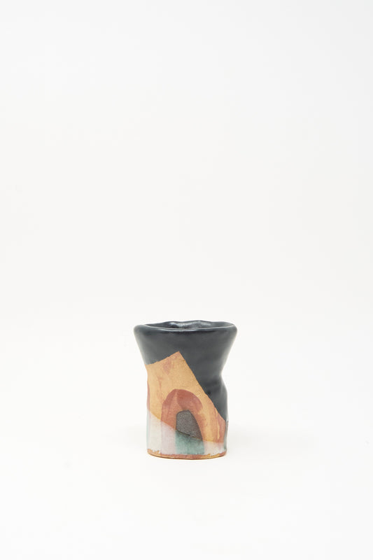 The "I wish I knew them Candleholder II" by Tamar Mogendorff is a small, uniquely shaped ceramic piece made in Brooklyn. With a black top and abstract patterns in beige, brown, and green adorning the lower half, this candleholder stands out for its artistic design. Set against a plain white background, it embodies the creative spirit characteristic of Tamar Mogendorff’s work.