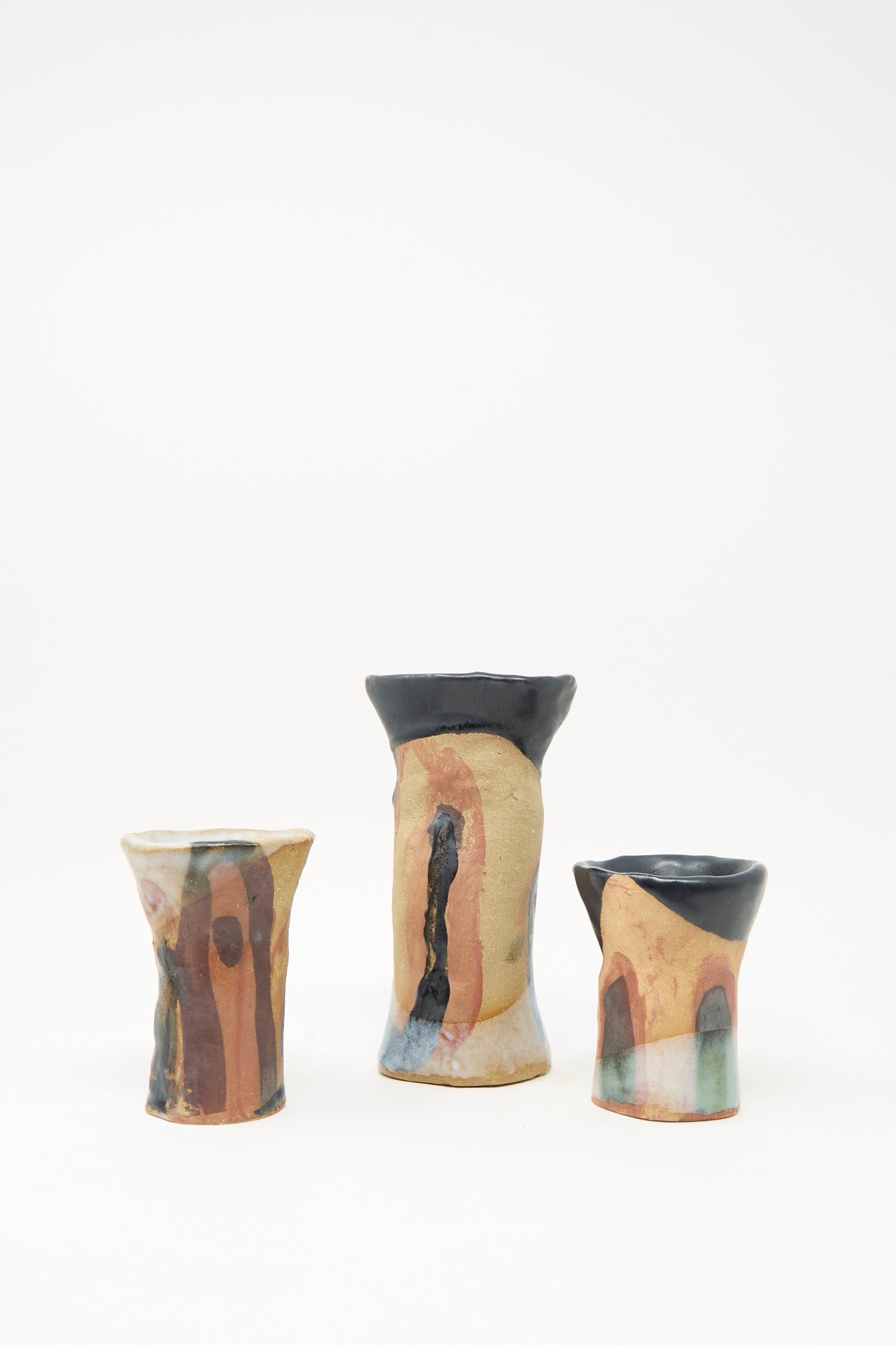 Three handmade "I wish I knew them Candleholder III" pieces by Tamar Mogendorff—crafted from Brooklyn ceramics with earthy, multicolored glazes and striking black and orange accents, each featuring a bold black rim—are artfully arranged against a plain white background.
