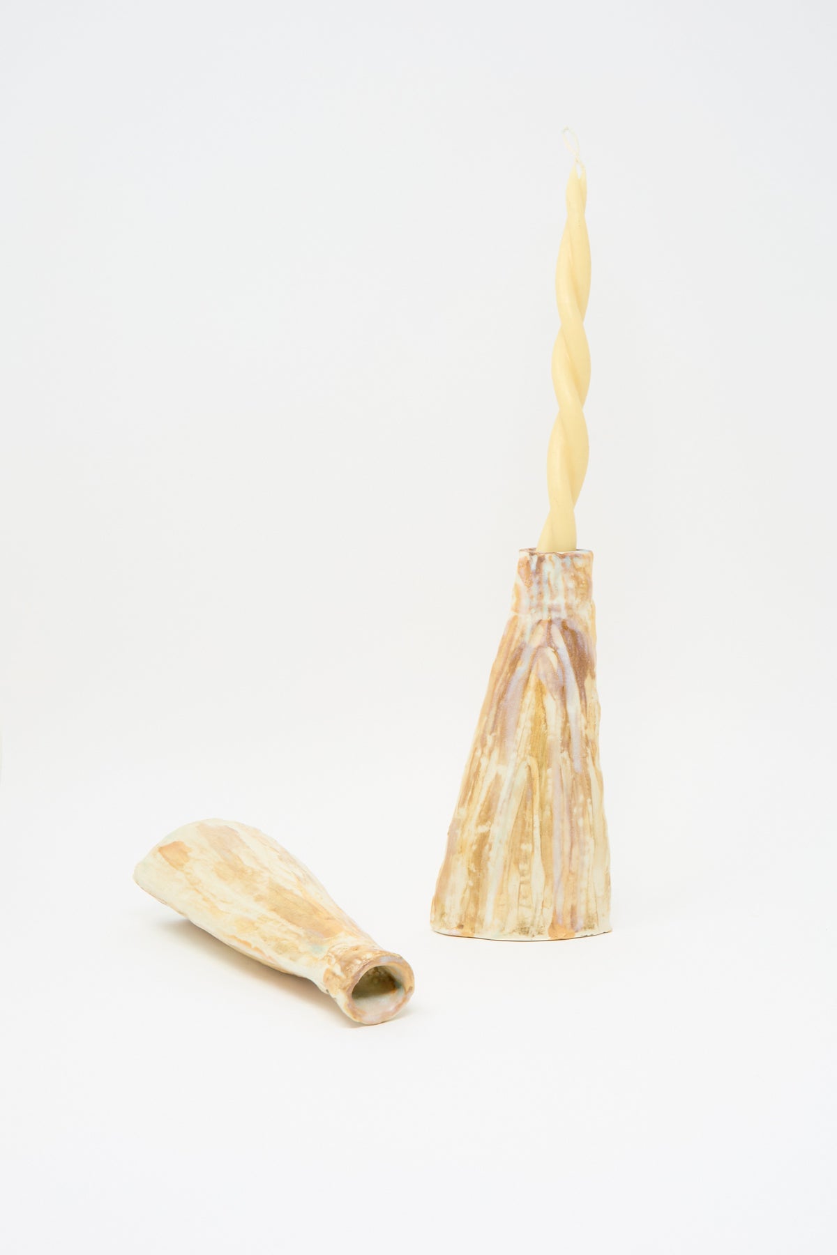 Tamar Mogendorff On Top of the Mountain Candle Holders Set: one textured handmade ceramic holder standing with a twisted taper candle and one lying on its side.