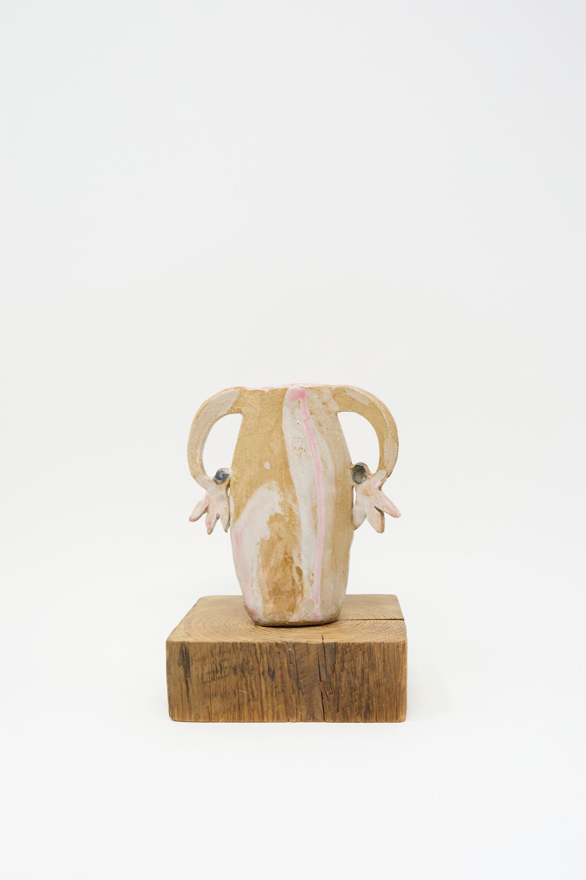 Tamar Mogendorff Pink Cyclamens Vase, a small handmade ceramic vessel with two handles and multicolored flower-shaped accents, sitting on a square wooden block.