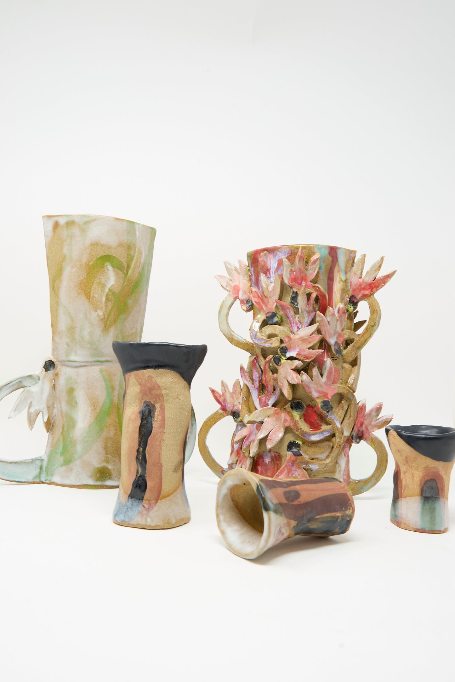 Five colorful ceramic vases with abstract patterns and organic shapes, including the handmade "Two Cyclamens by the Lake Vase" by Tamar Mogendorff, adorned with pink flower-like decorations, arranged on a plain white background.