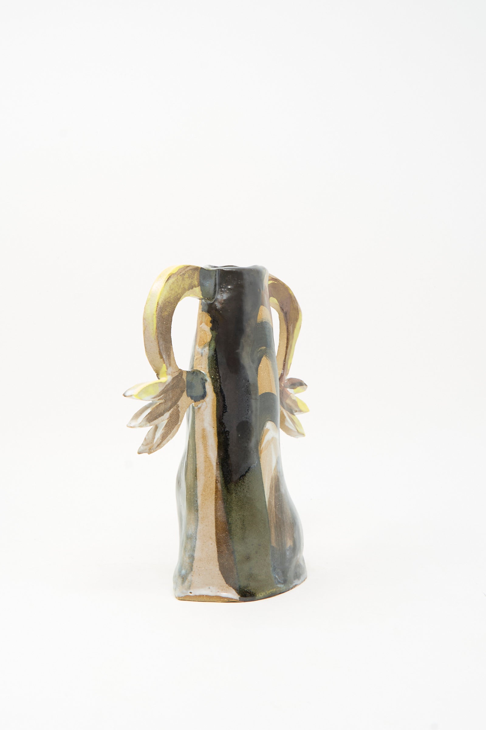 The "Two Cyclamens on Top of a Mountain Vase" by Tamar Mogendorff is a handmade ceramic piece featuring a wavy, uneven surface, two yellow-brown curved handles, and leaf-like decorations on each side. Set against a plain white background, this unique vase captures Brooklyn-inspired artistry.