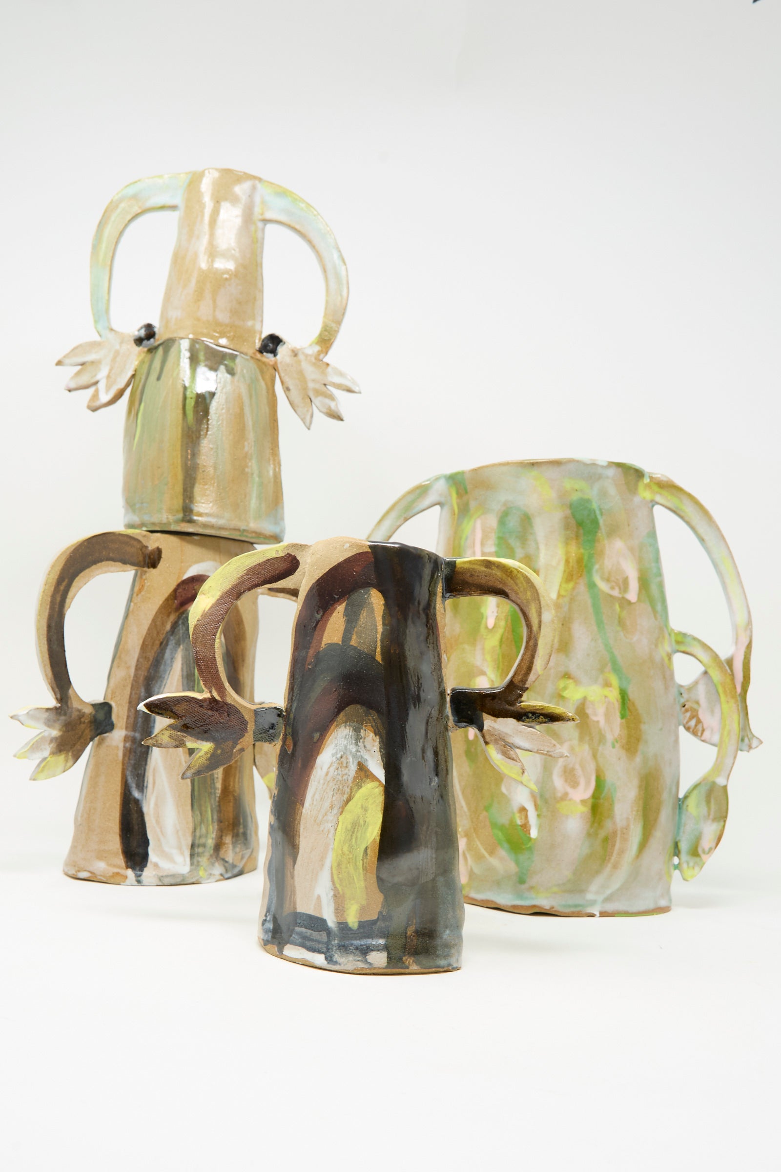 Three "Two Cyclamens on Top of a Mountain" vases by Tamar Mogendorff, featuring abstract, earth-tone designs and curved handles reminiscent of handmade ceramics, are displayed against a plain white background.