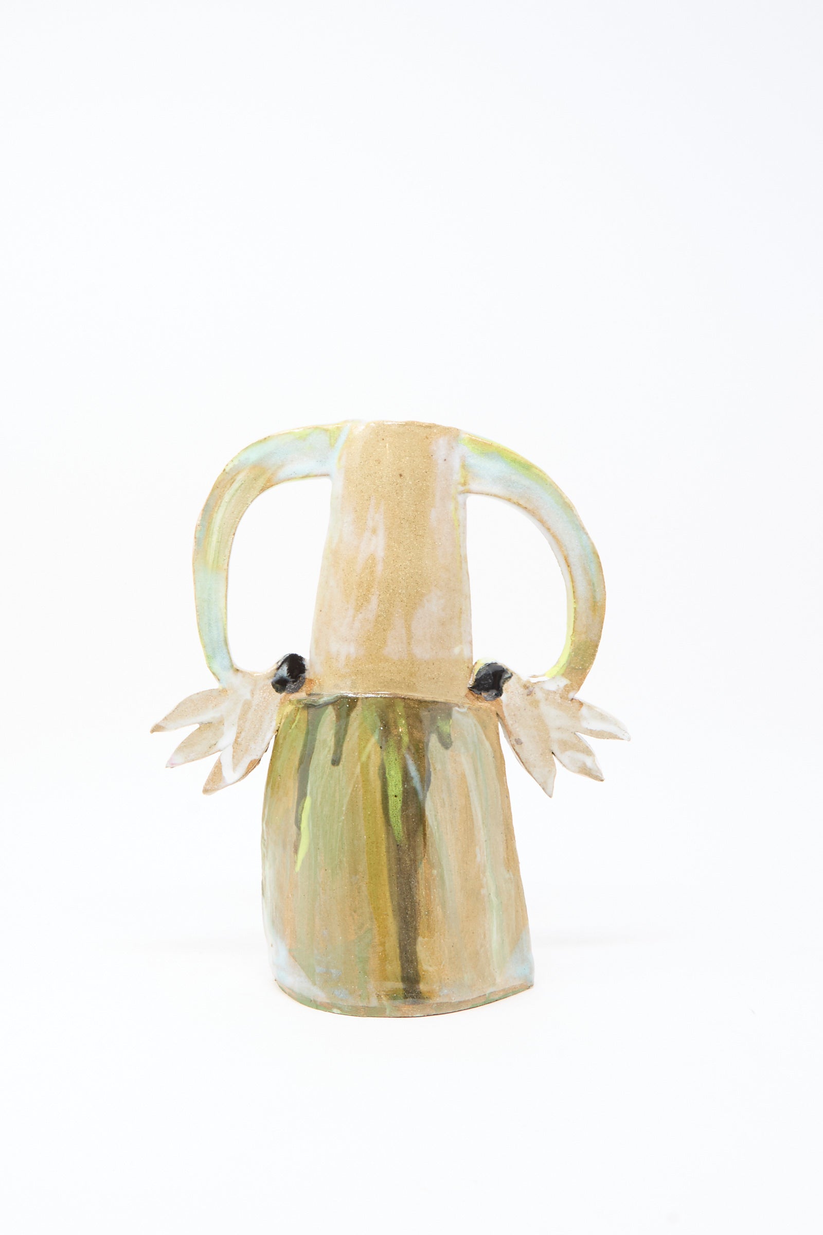 The "Two Cyclamens on Top of a Mountain Vase III" by Tamar Mogendorff is a handmade Brooklyn ceramic vase with two handles, pale earth tones, and wing and eye motifs on each side, set against a white background.