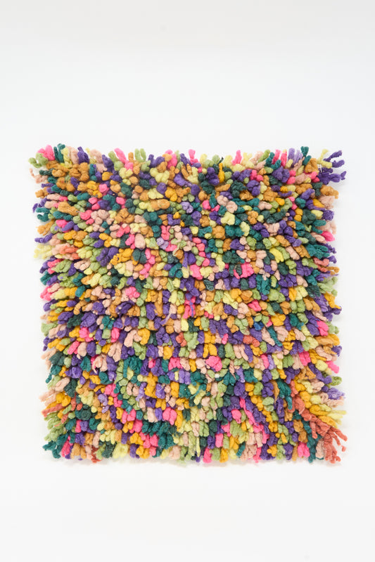 The Chair Rug in Mixed Colors by Tamar Mogendorff is a square, multicolored textured yarn art piece with a shaggy, tufted surface on white, reminiscent of handwoven Guatemalan wool rugs.