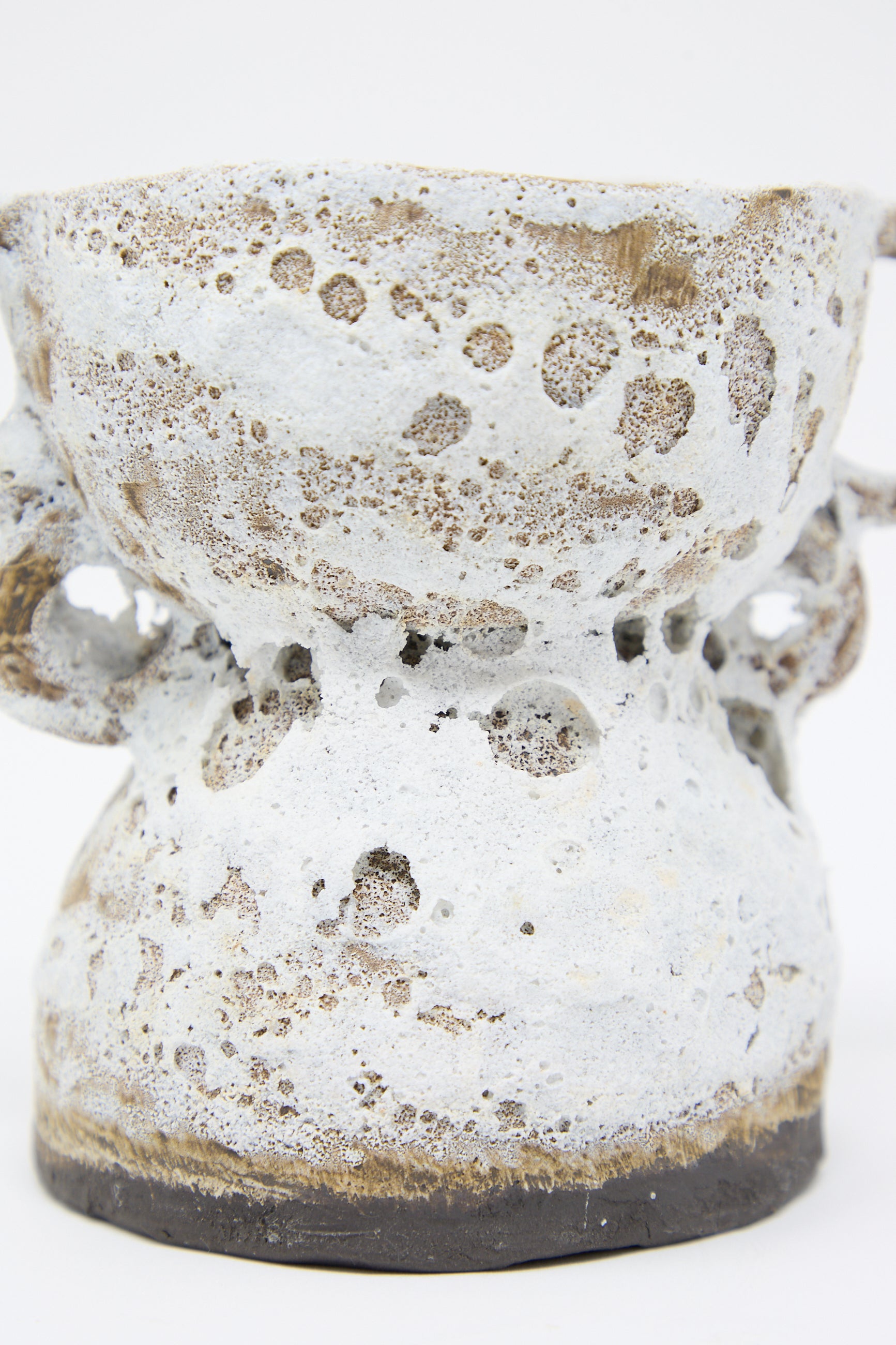 A close-up of The Ancient One Vase by Tania Whalen, showcasing its textured, white and brown stoneware body with a bulbous shape, rough, porous surface, and a tiered design with handles.
