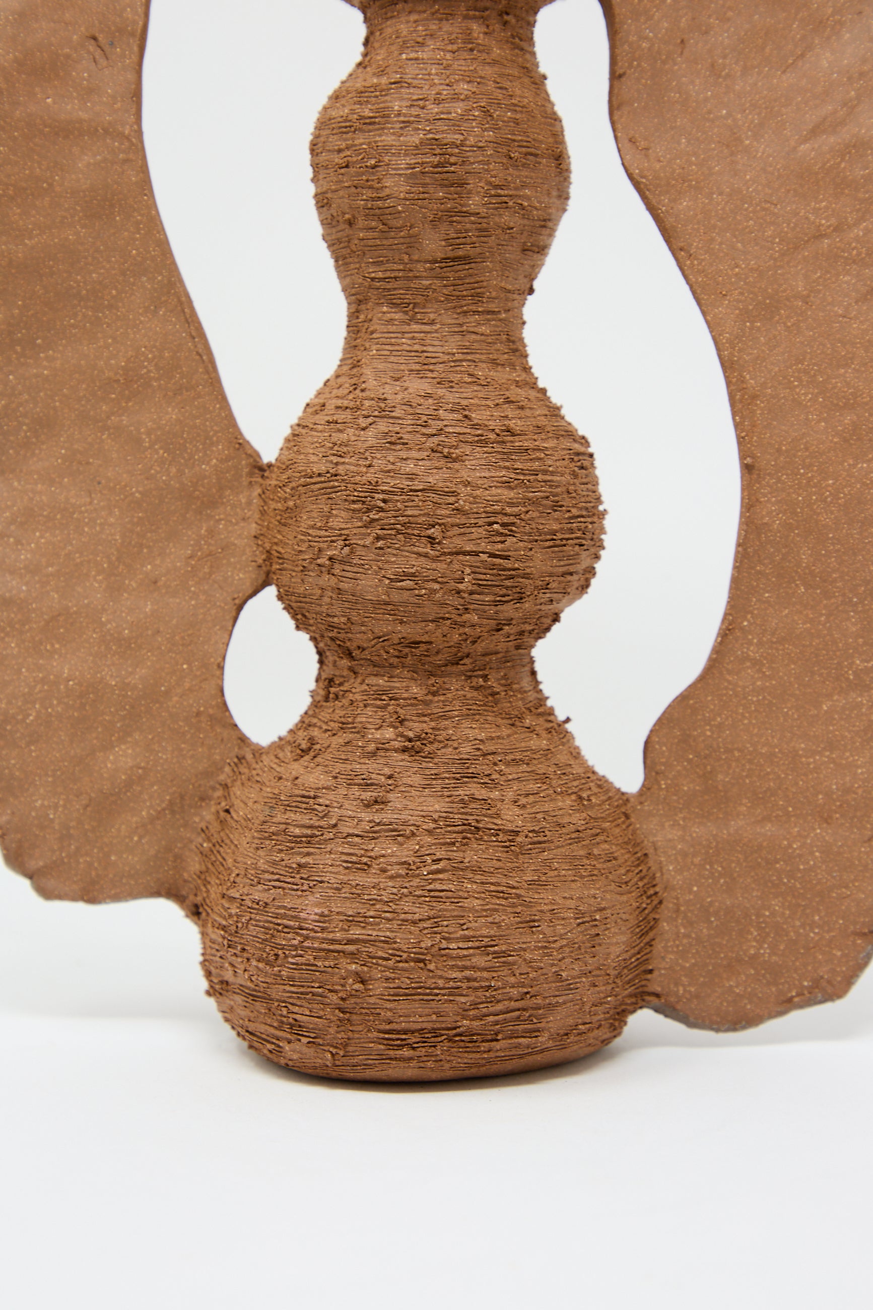 A textured sculpture with three stacked, spherical shapes and wing-like extensions, crafted from a material resembling clay or wood, evokes the charm of The Flying Ra Vase by Tania Whalen, set against a plain white background.