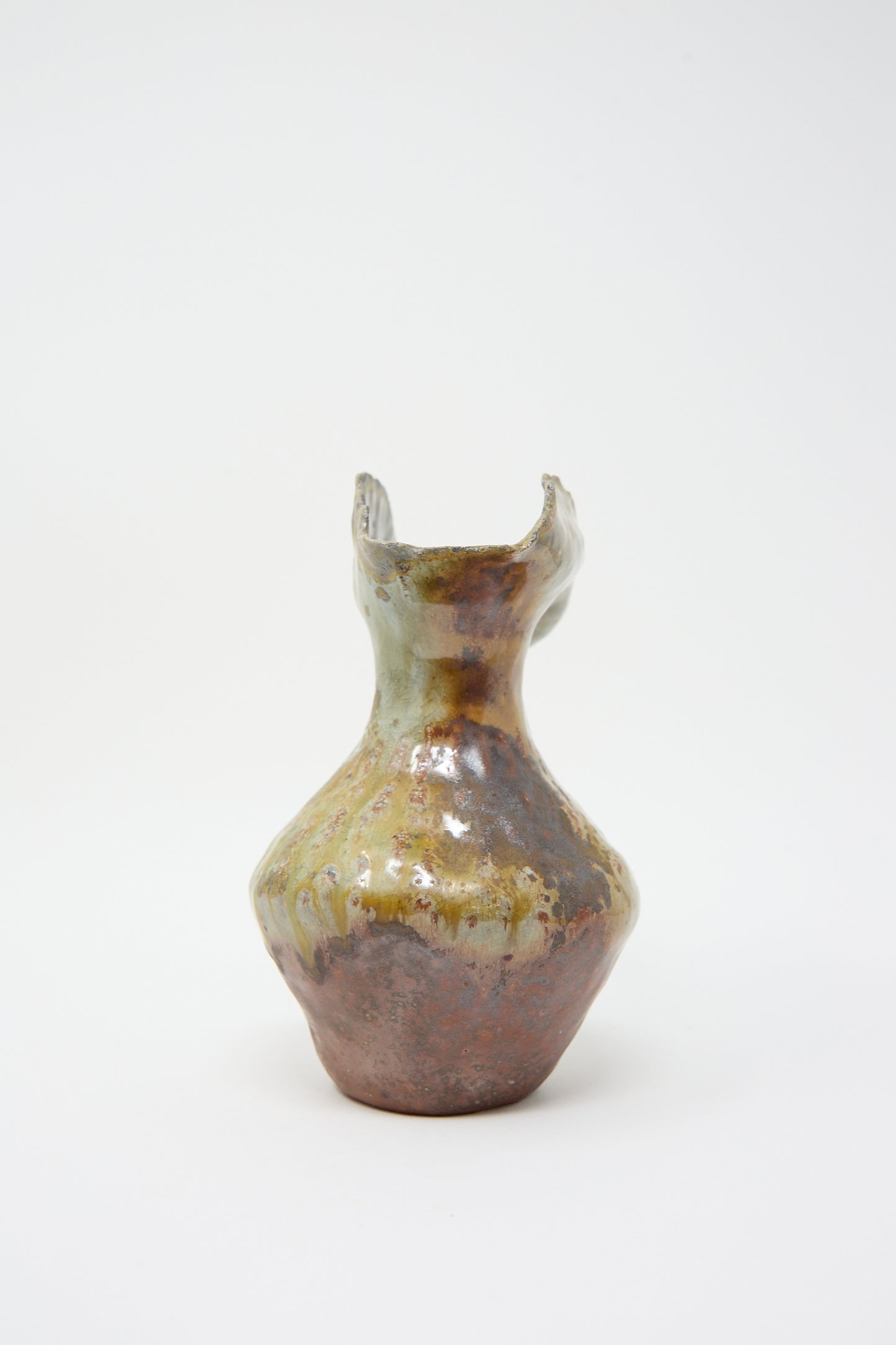 Hand-built ceramic vase with a narrow neck, ruffled opening, and mottled green, brown, and cream glaze is now available as The Small Woodfired Flutter Vase by Tania Whalen.