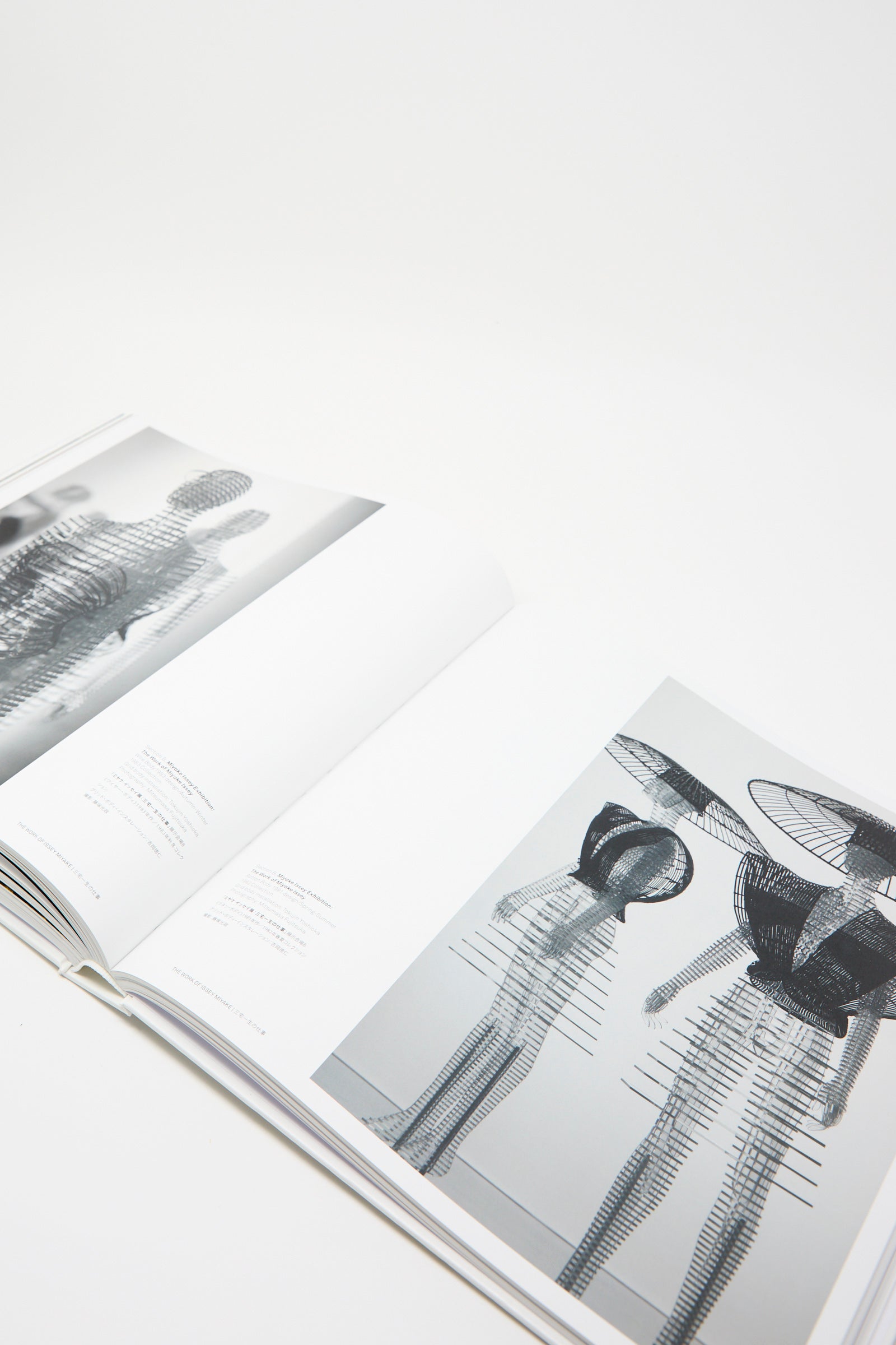 An opened page of the book, produced by Taschen, displays black and white abstract sculptures on its pages, encapsulating the vision of Issey Miyake. Photographed against a black background. 