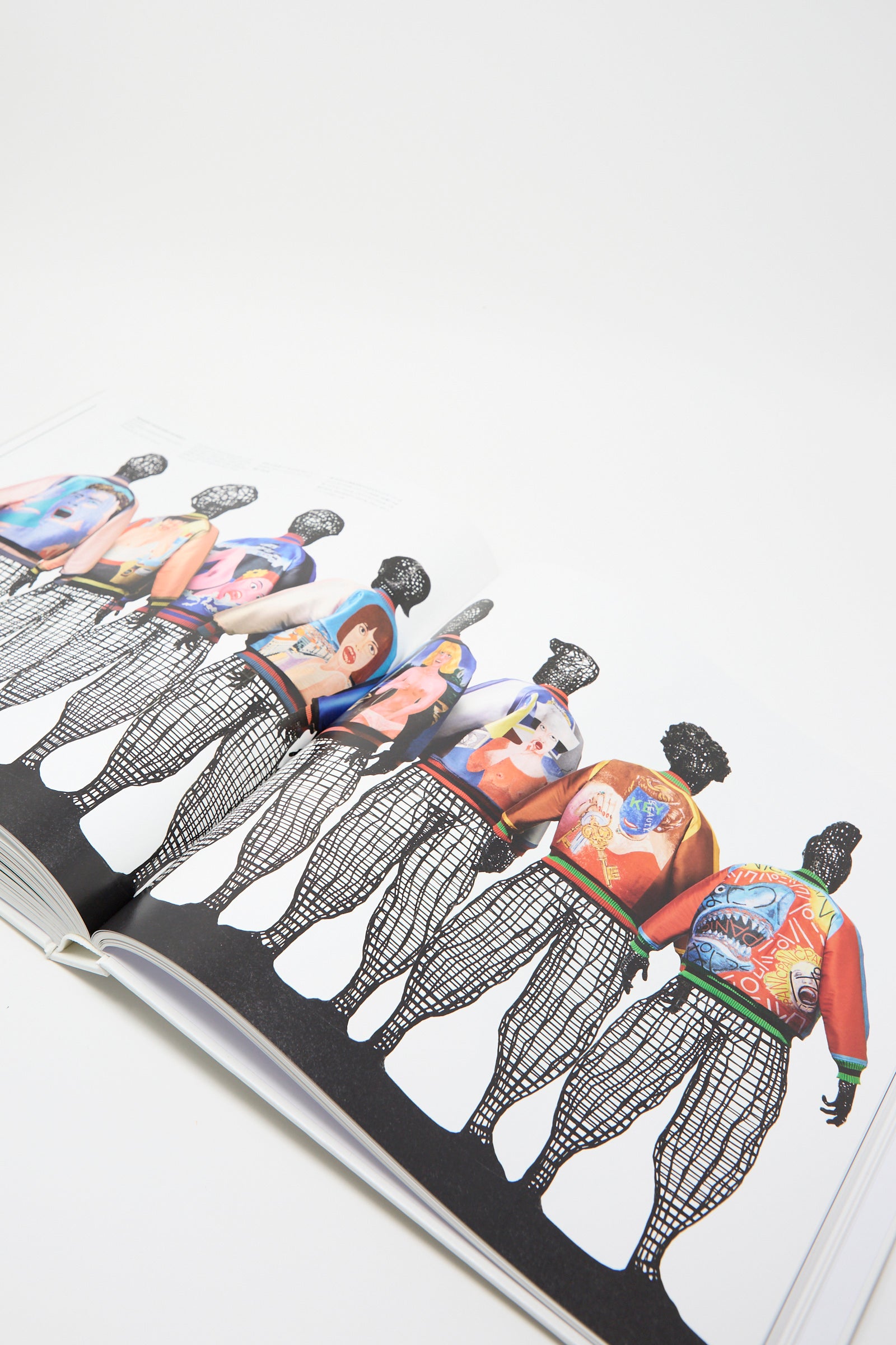 The open page of Taschen's book showcases a series of figures, each dressed in vibrant, artistic designs that reflect Issey Miyake's vision. Set against a white background. 