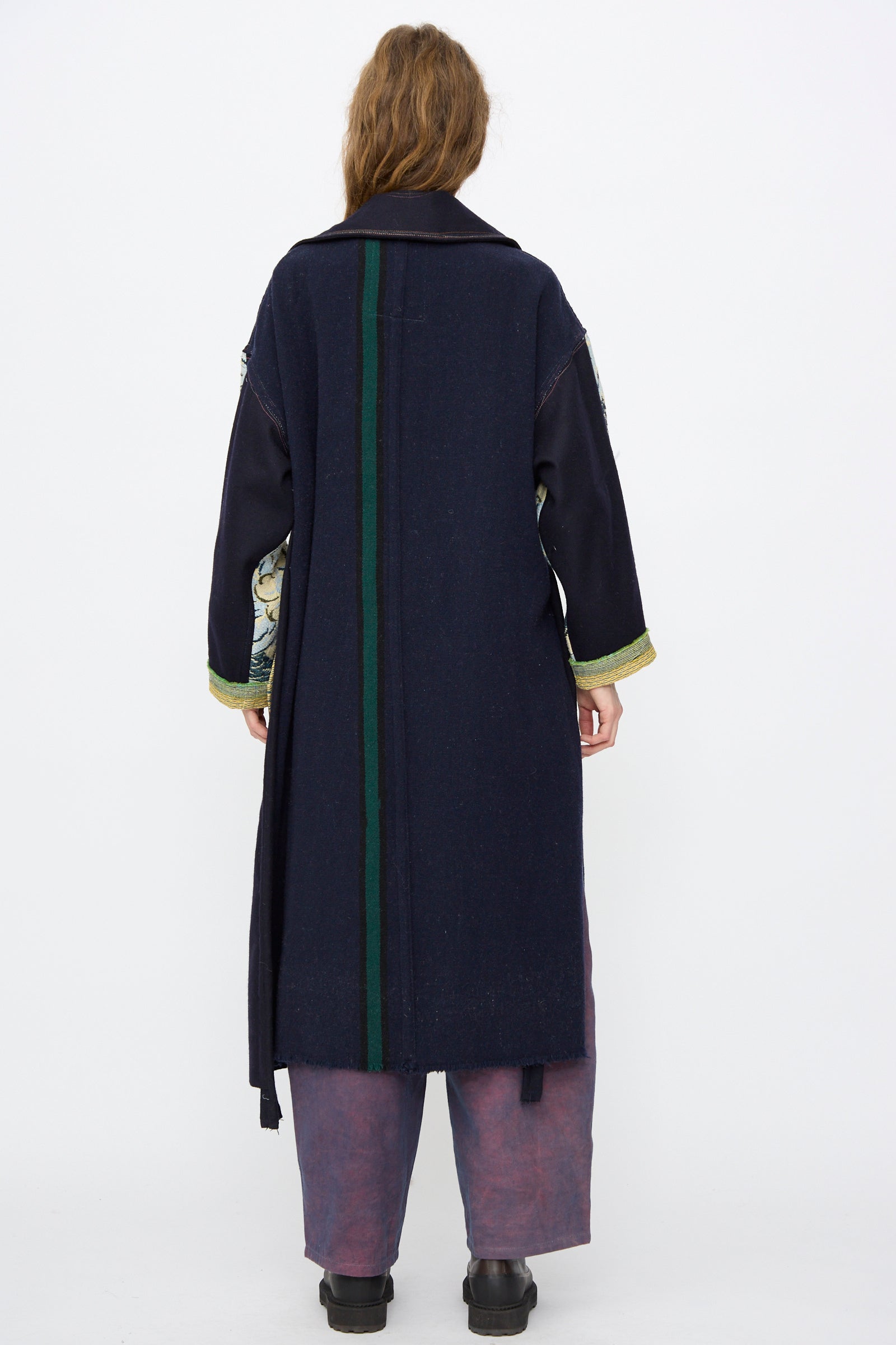 A person stands with their back to the camera, wearing the Thank You Have A Good Day Crosby Coat in navy with a green center stripe, featuring an oversized fit over wide-legged pants and black shoes.