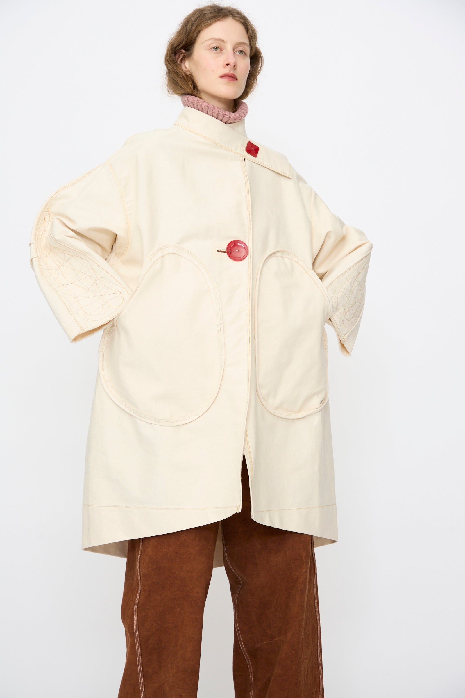 A person wears the Thank You Have A Good Day Denim Fishtail Parka in Ecru, brown wide-leg pants, and a pink turtleneck sweater, standing against a plain white background.