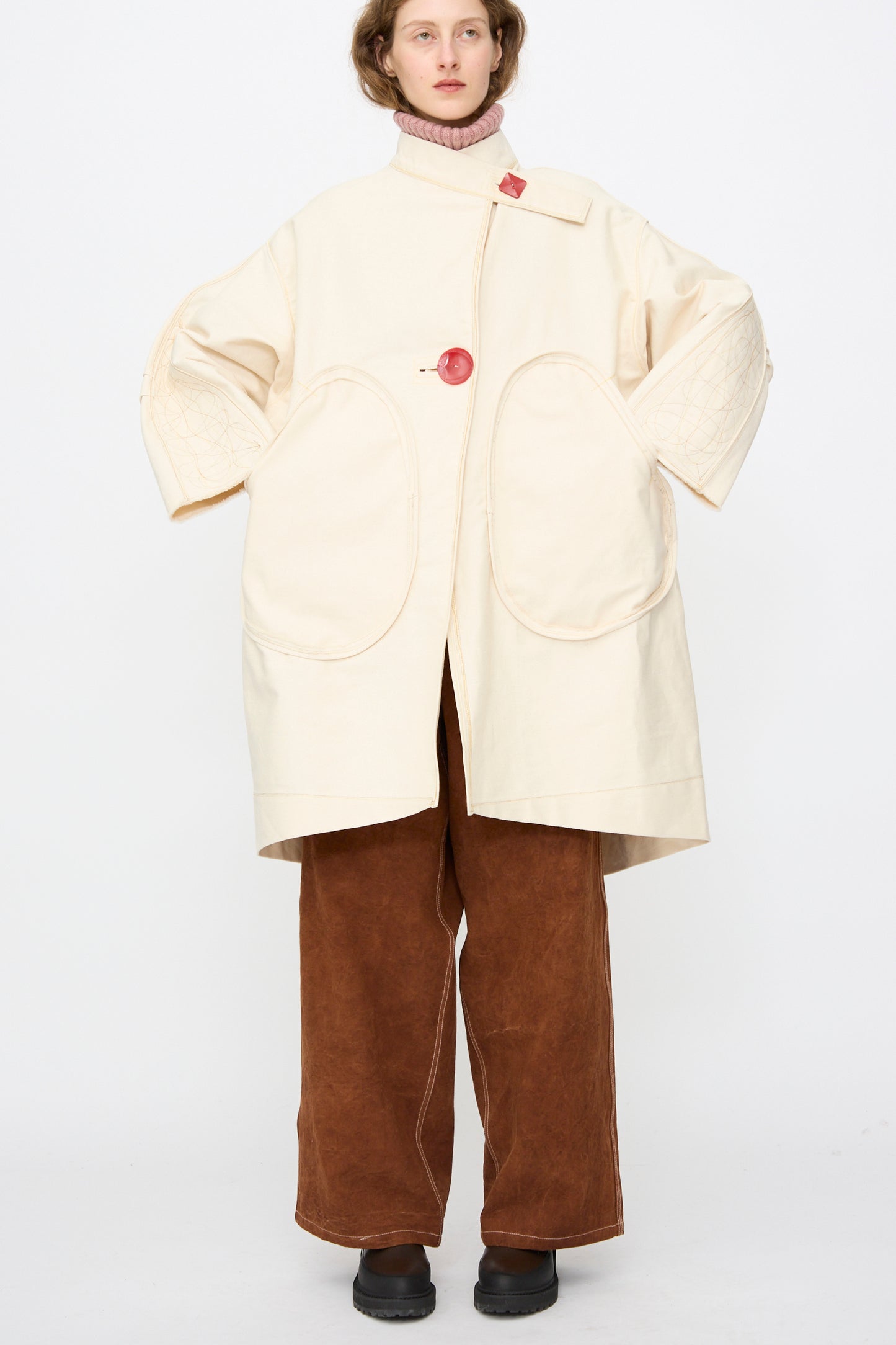 A person wears the Thank You Have A Good Day Denim Fishtail Parka in Ecru, styled with a pink turtleneck, wide brown pants, and black shoes, standing against a plain white background.