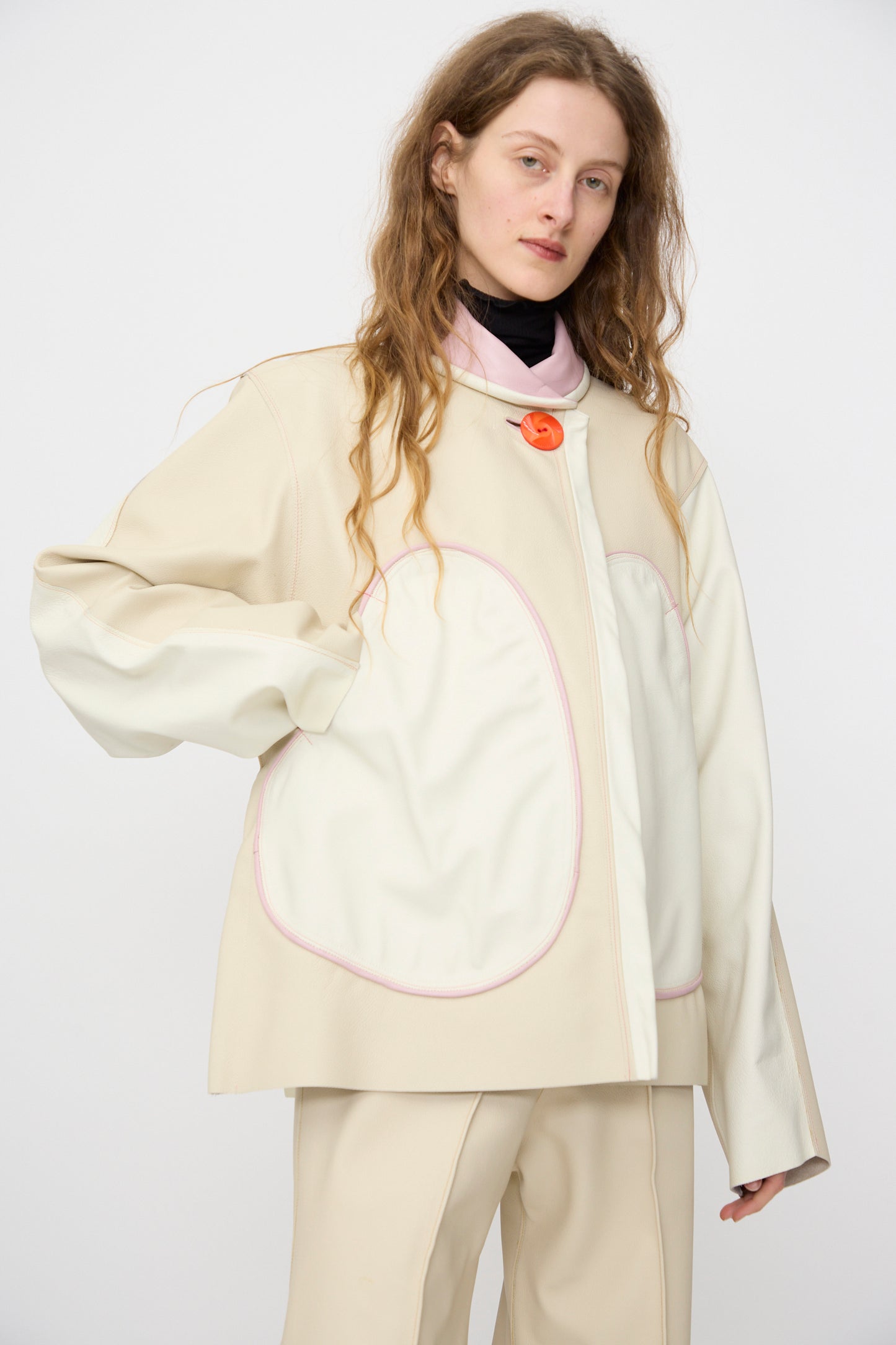 A person with long hair wears the Leather Chore Jacket in Ecru by Thank You Have A Good Day, with oversized white pockets, a pink collar, and a single orange button—handmade in NYC.