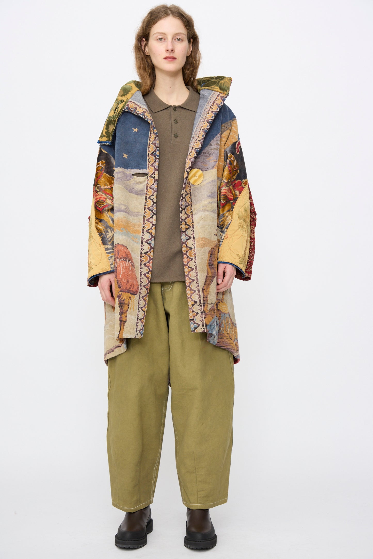A person faces forward in a Thank You Have A Good Day Scenic Tapestry Fishtail Parka, styled with olive green pants, a brown top, and black boots against a plain white background.
