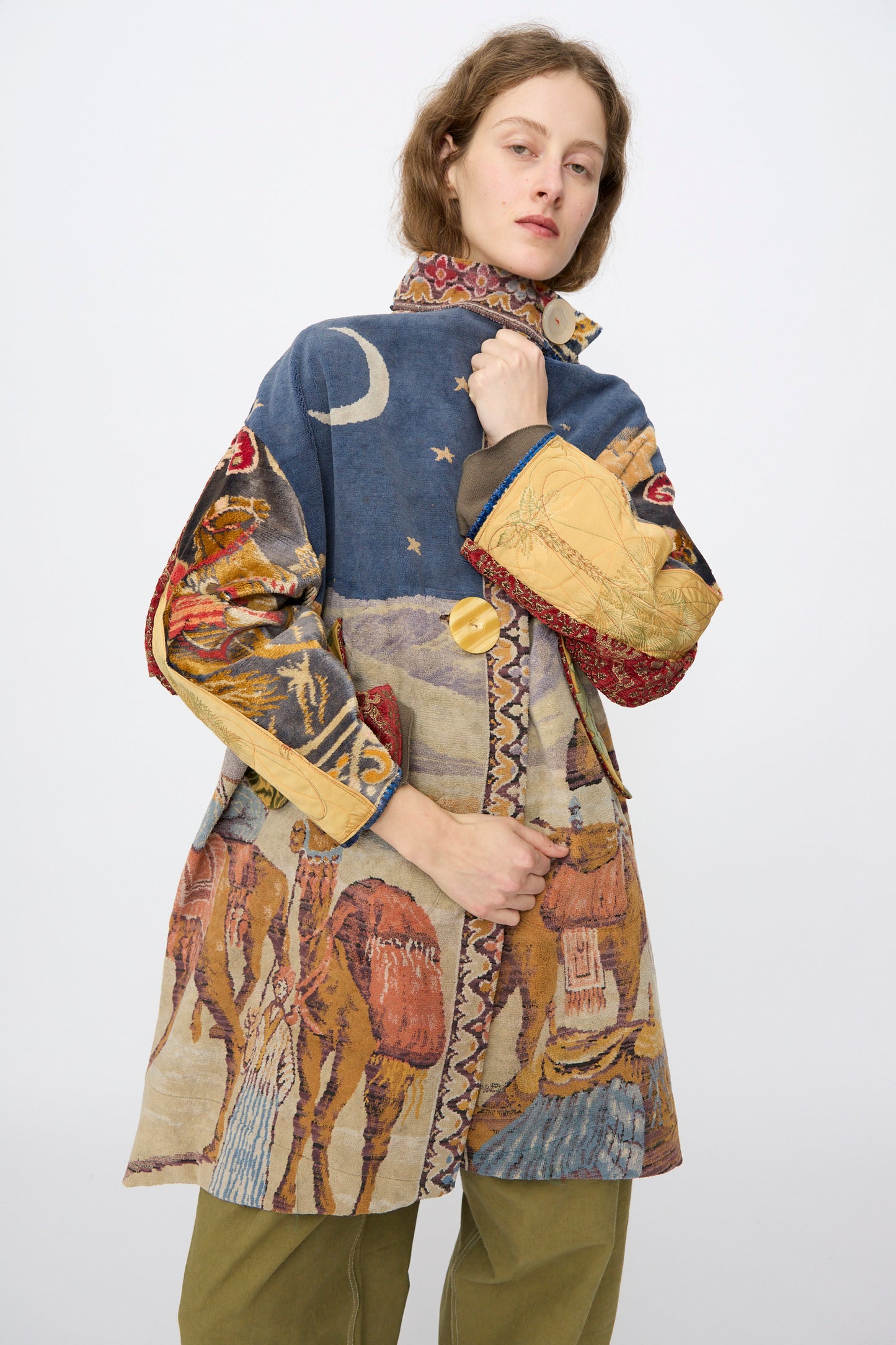 A person wears the Scenic Tapestry Fishtail Parka by Thank You Have A Good Day, featuring moons, stars, and camels, standing against a plain light background.