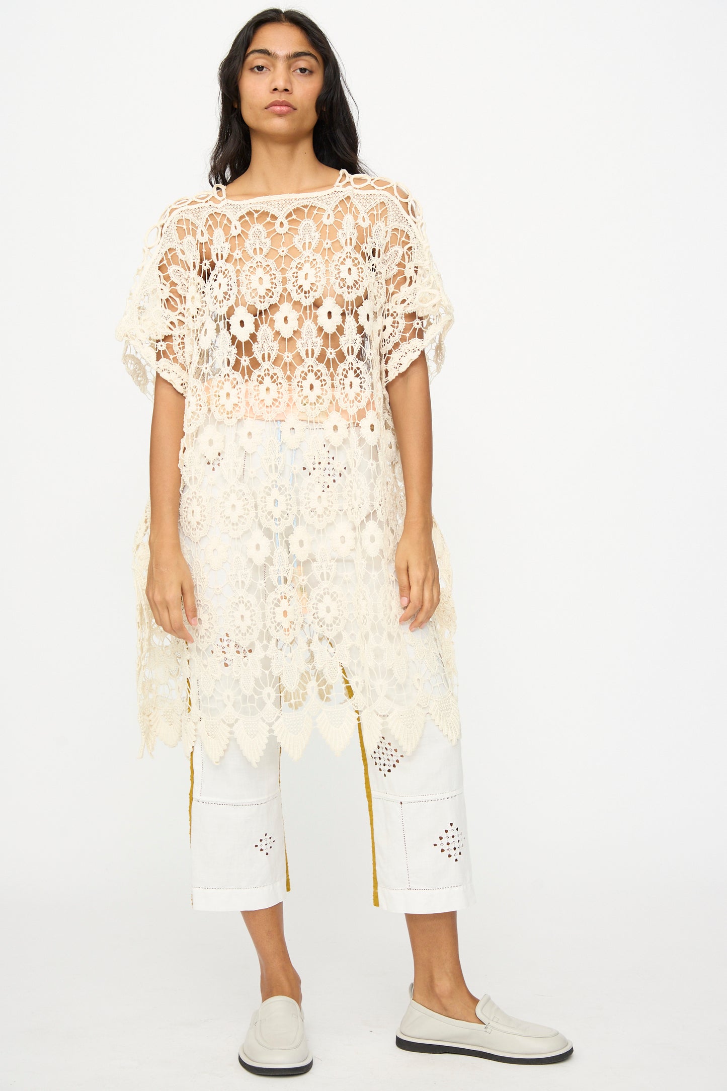A person stands facing forward in a Thank You Have A Good Day Antique Lace Midi Caftan, layered over white cropped pants and white slip-on shoes, set against a plain background.